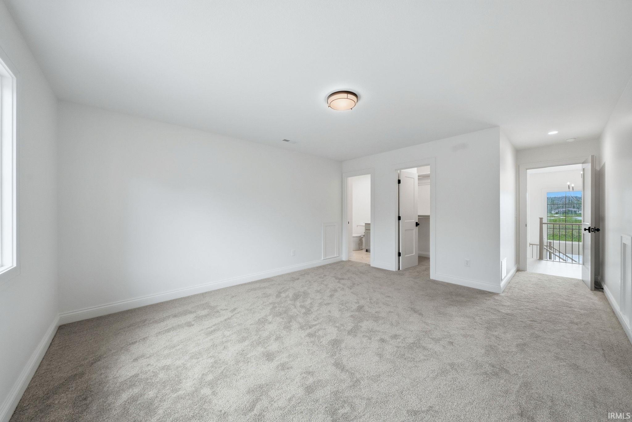 Expansive carpeted room featuring white painted walls, a window with white trim, a semi-flush mount ceiling light, and multiple interior doors