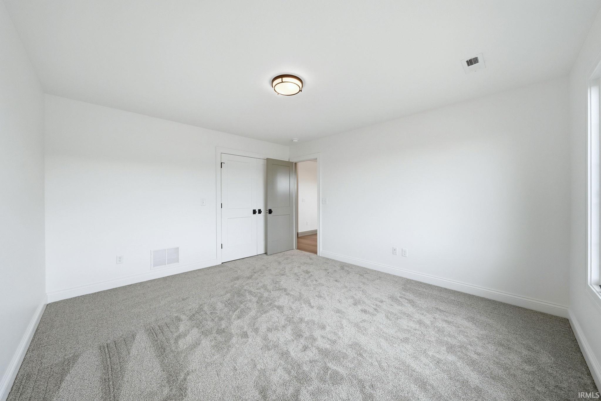 Carpeted room featuring white walls, a flush-mount ceiling light fixture, and a window providing natural illumination