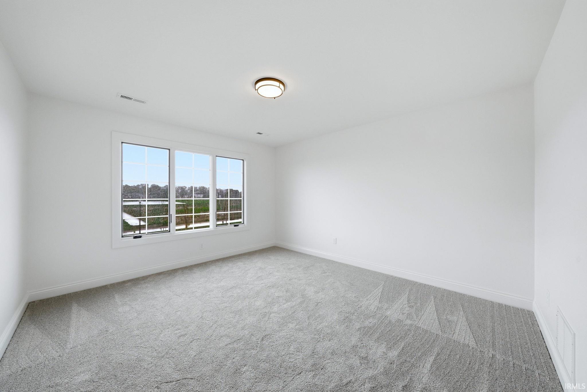 Bright room featuring three large windows with white frames, offering views of a distant body of water and surrounding greenery