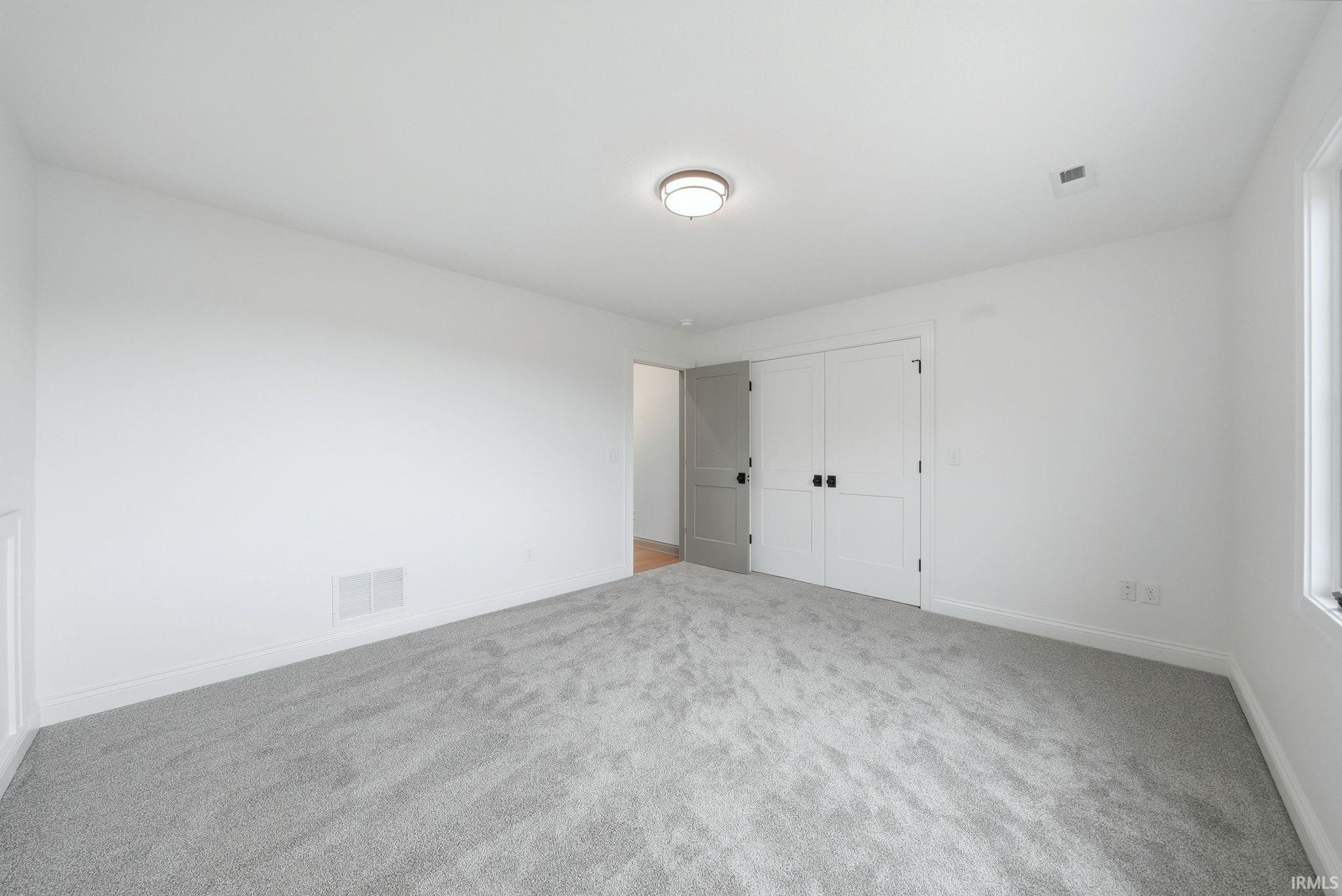 Spacious room featuring light gray carpeting, white walls, and a contemporary ceiling light fixture