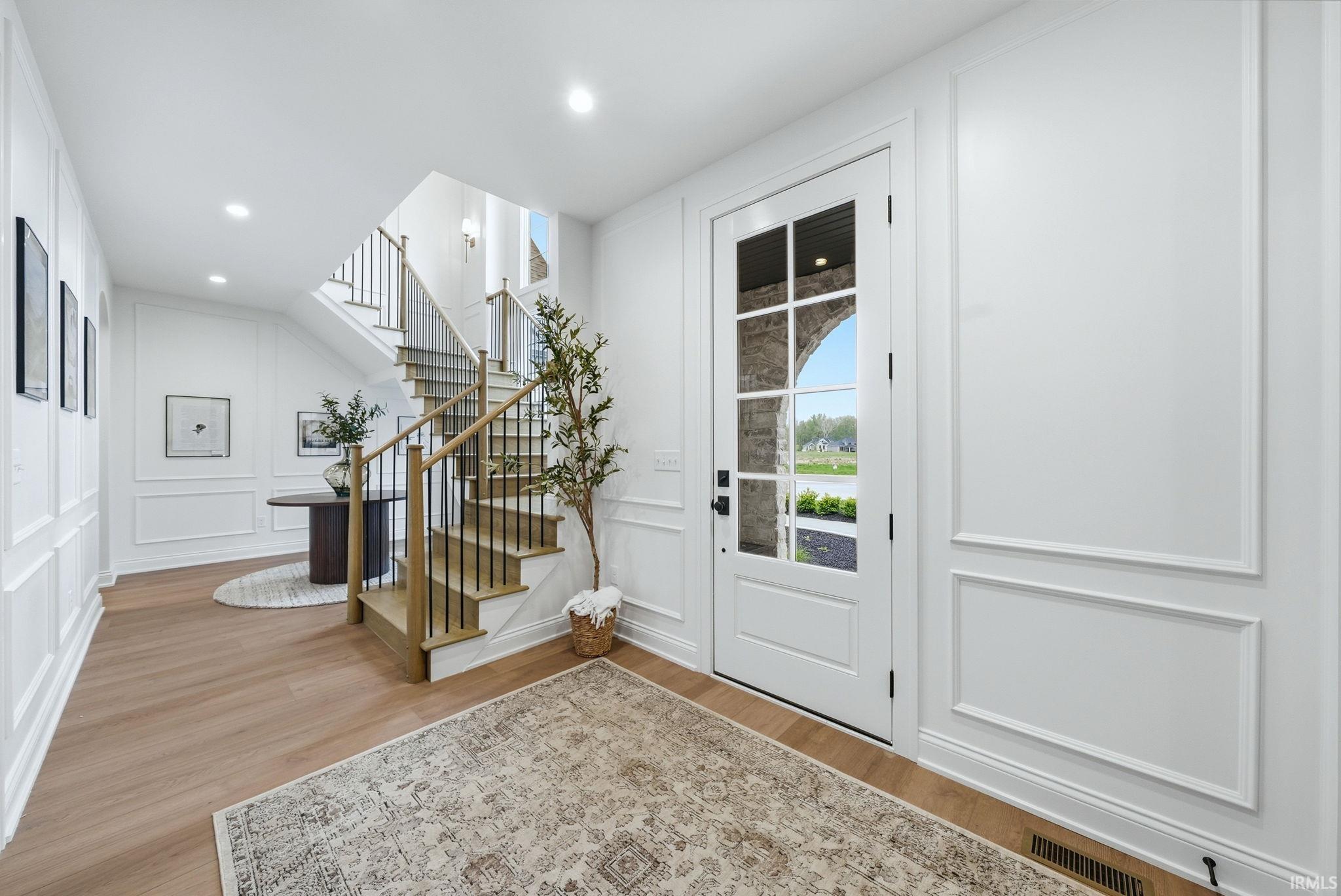 Foyer featuring wood-finish flooring, wainscoting, and a staircase with light wood treads and black metal balusters