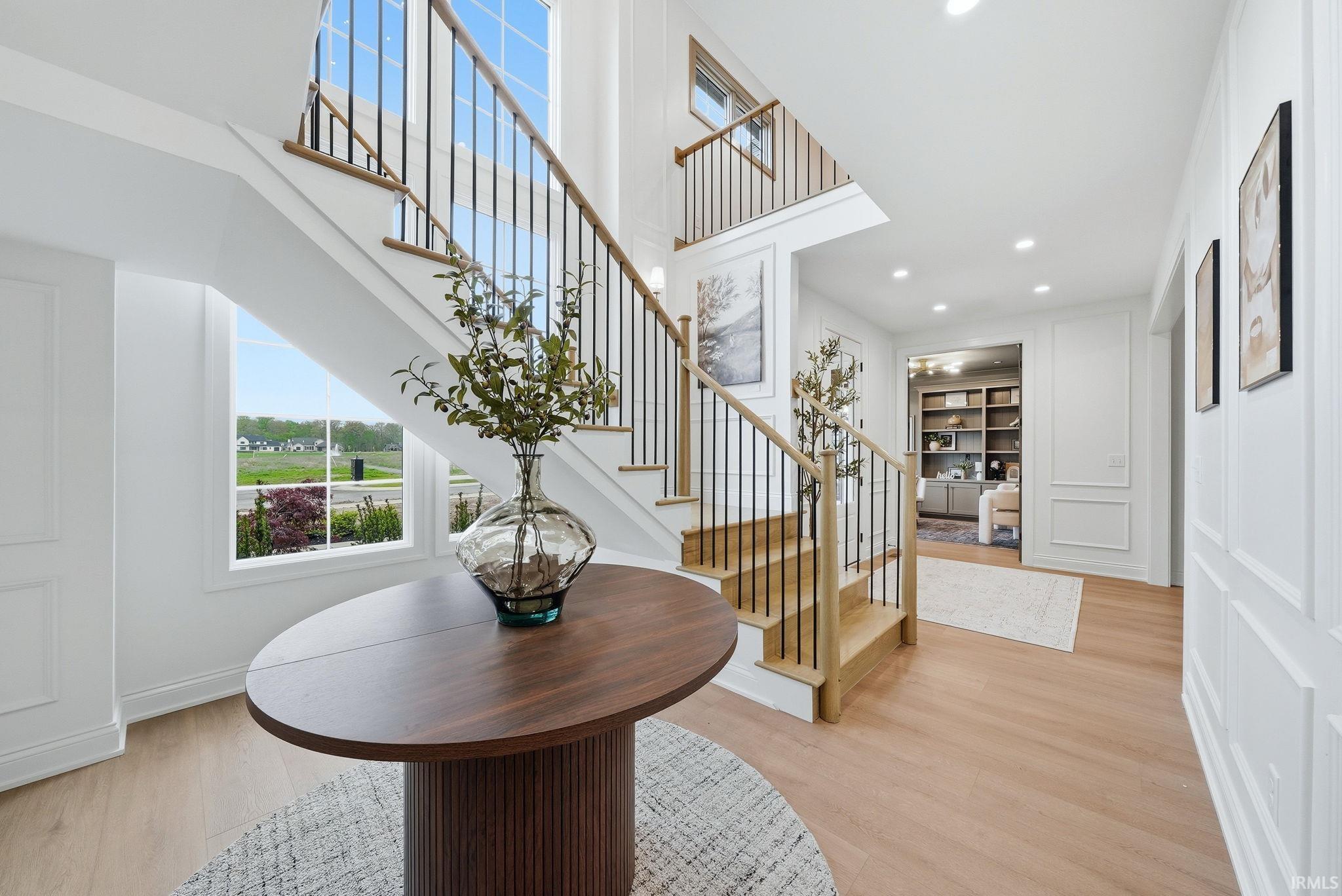 Two-story foyer featuring a grand staircase with wrought iron balusters and wood handrails, hardwood flooring, wainscoting, and large windows