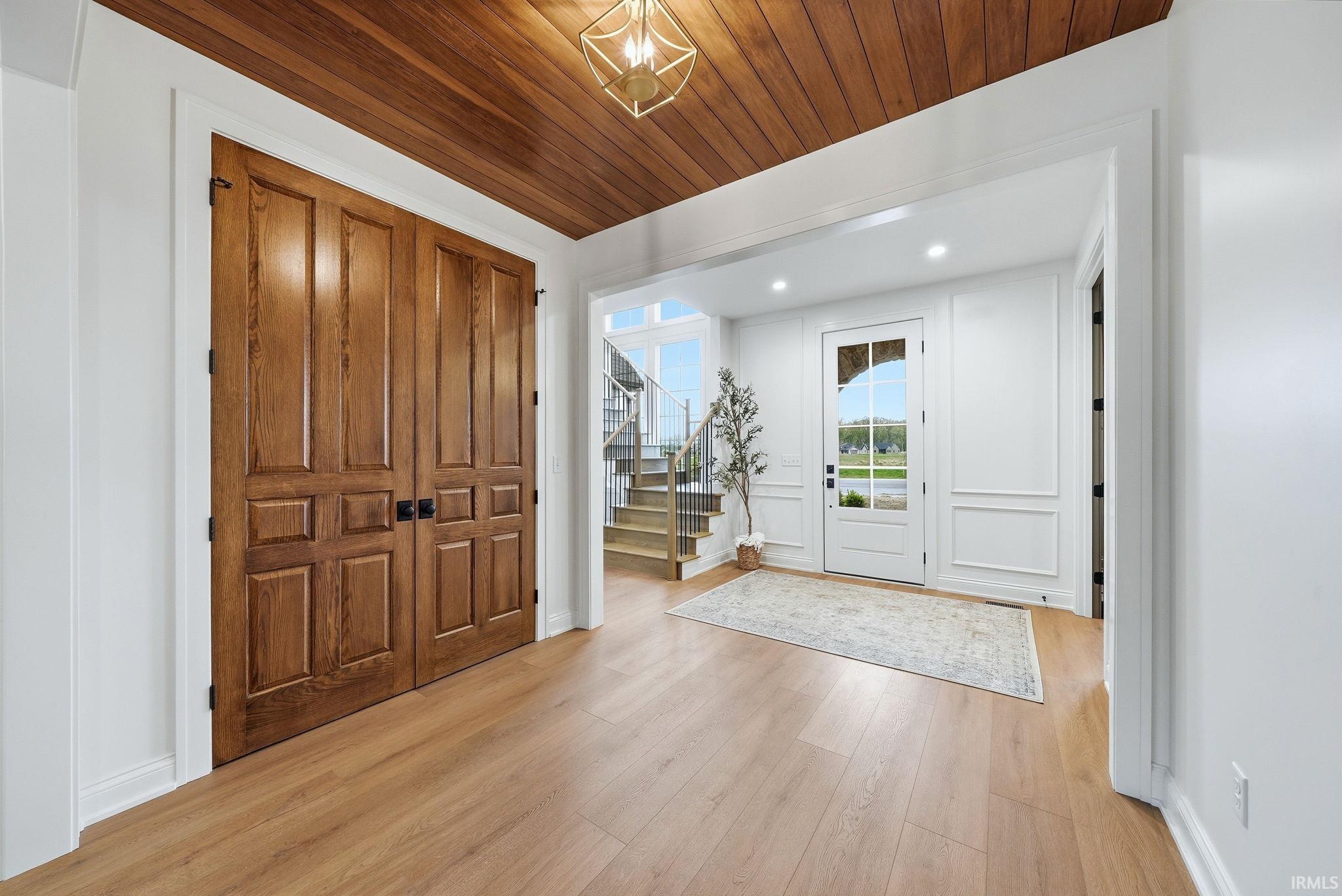 Entryway featuring light wood-finish flooring, a paneled wood ceiling, and a white paneled door with glass inserts