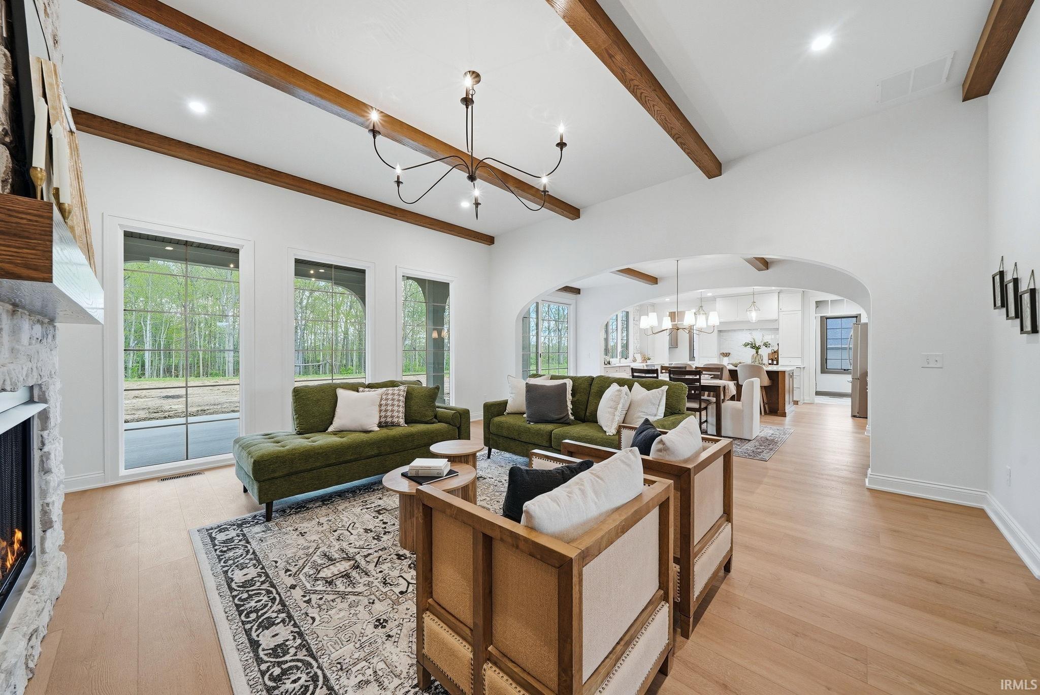 Spacious living area featuring exposed wood beams, a vaulted ceiling, wood-finish flooring, a stone-clad fireplace, and multiple arched windows