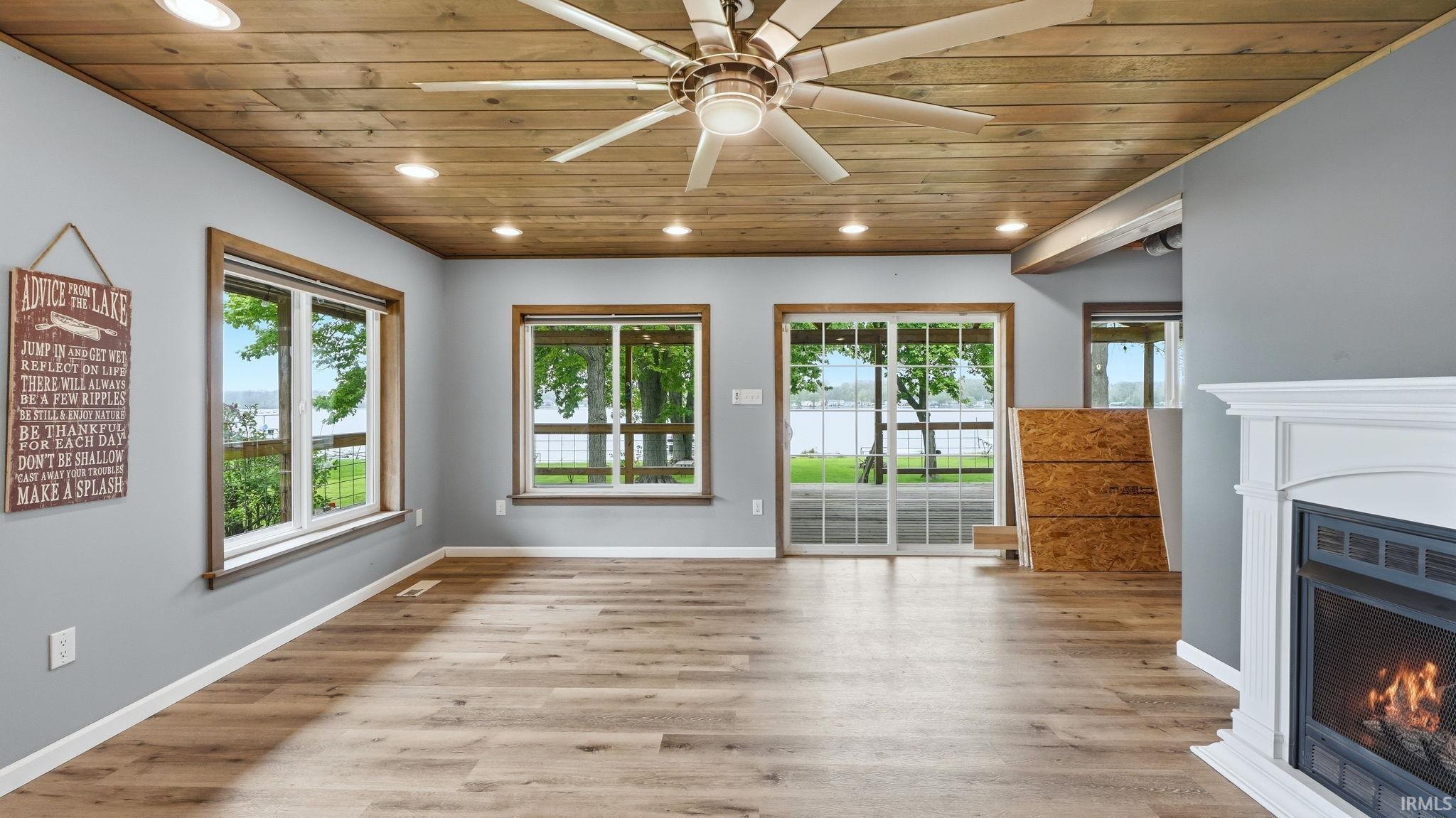 Spacious living area featuring wood-finish flooring, a white fireplace with a dark insert, and a wood plank ceiling with recessed lighting and a ceiling fan