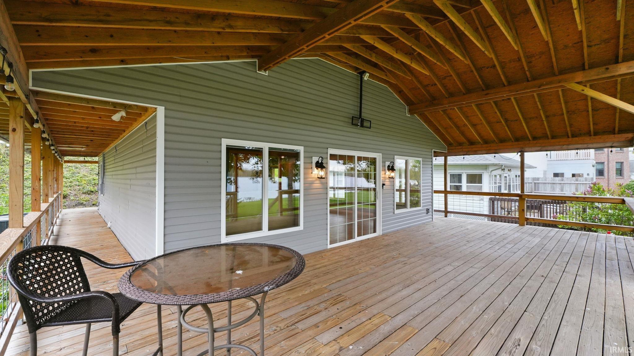 Expansive covered deck featuring wood decking, an exposed wood beam ceiling, and a light gray siding exterior