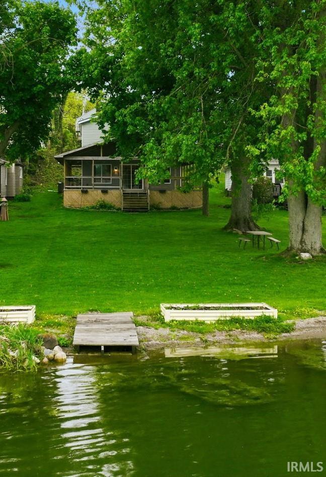 Waterfront property featuring a screened porch, wood stairs, lush green lawn, and mature trees