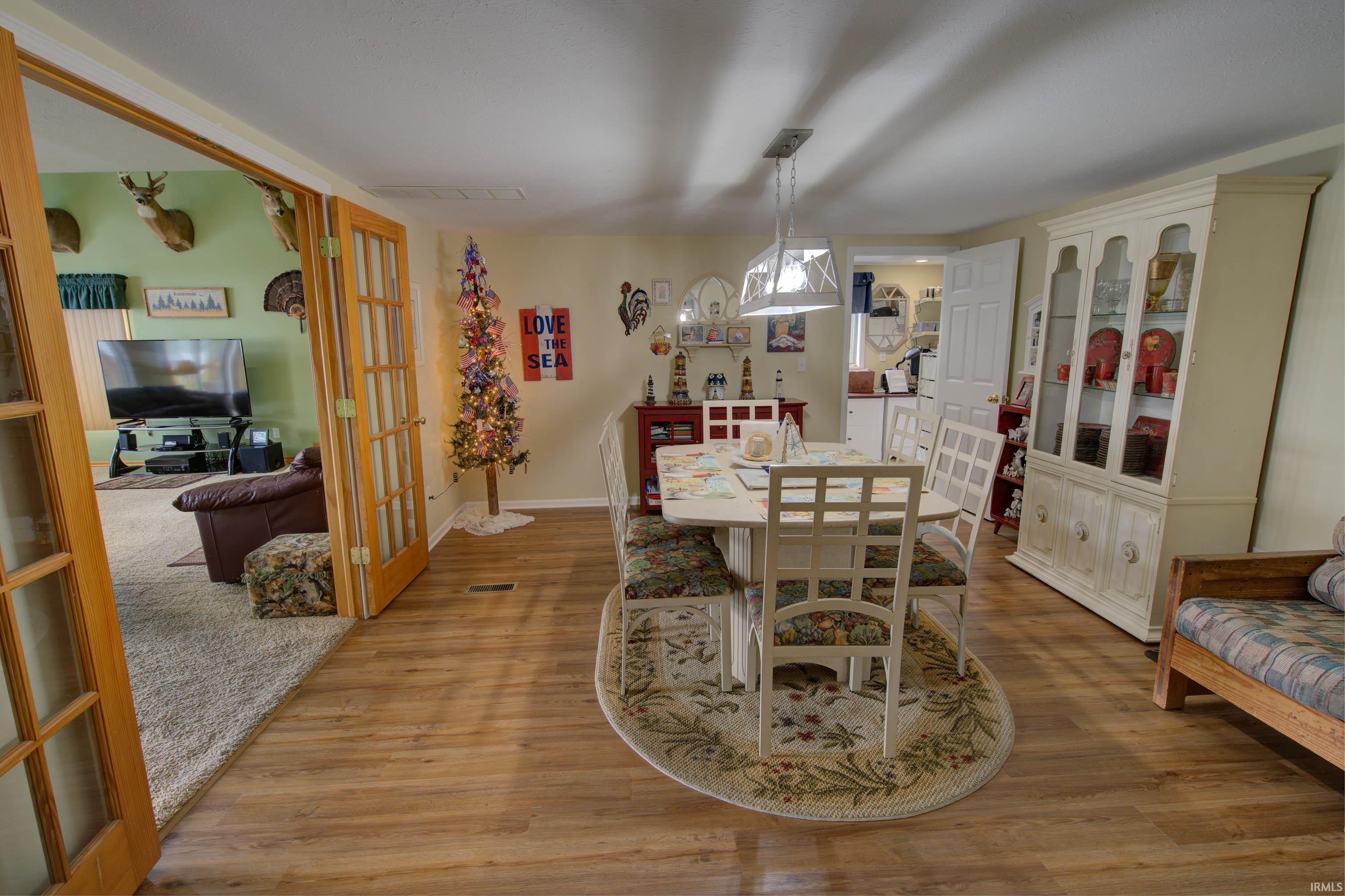 Dining area featuring wood-finish flooring, a contemporary chandelier, and French doors opening to a carpeted room