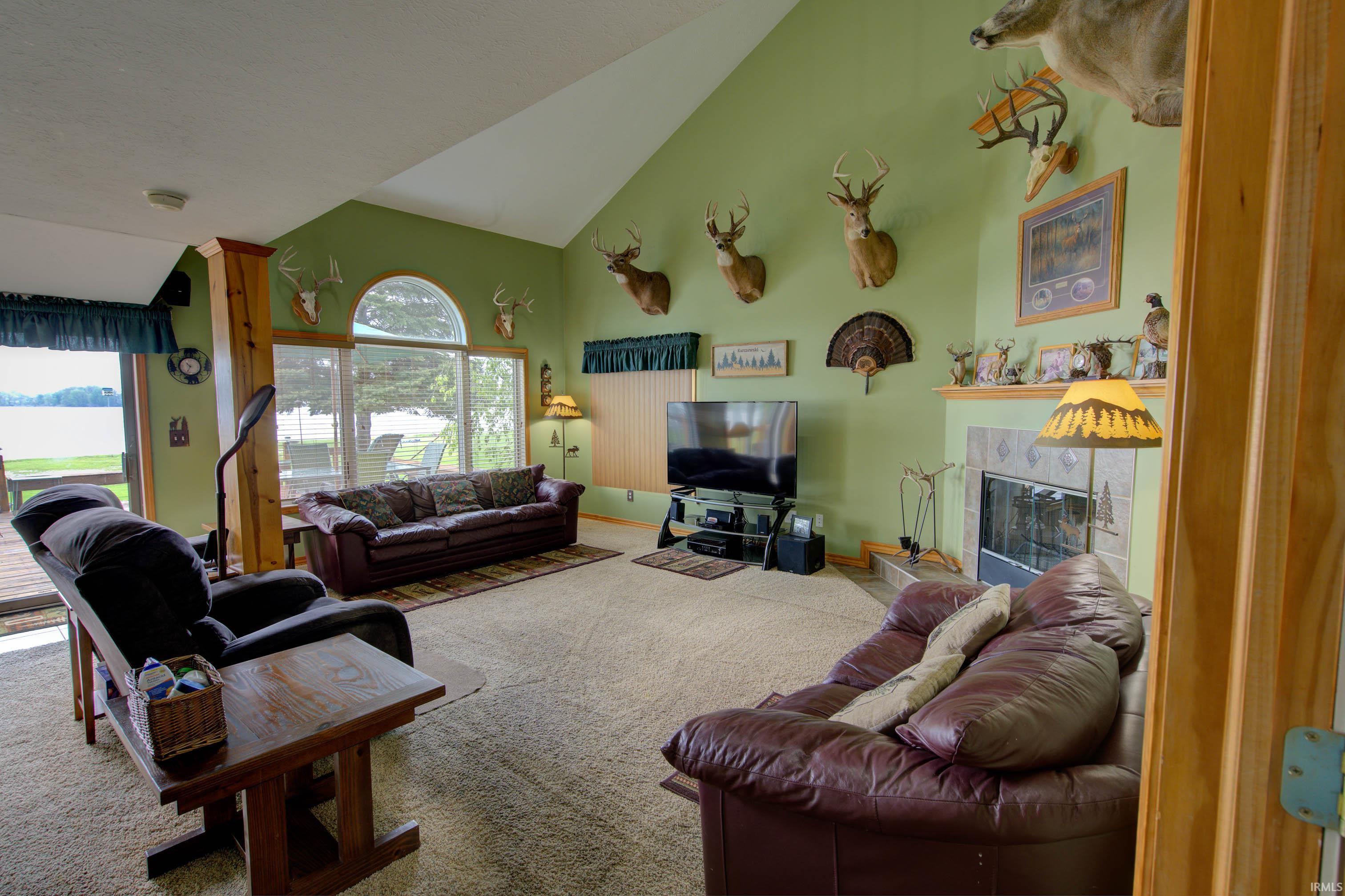 Vaulted ceiling living area featuring a fireplace with a tile surround and mantel, a sliding glass door to an outdoor deck, and large picture windows with an arched transom