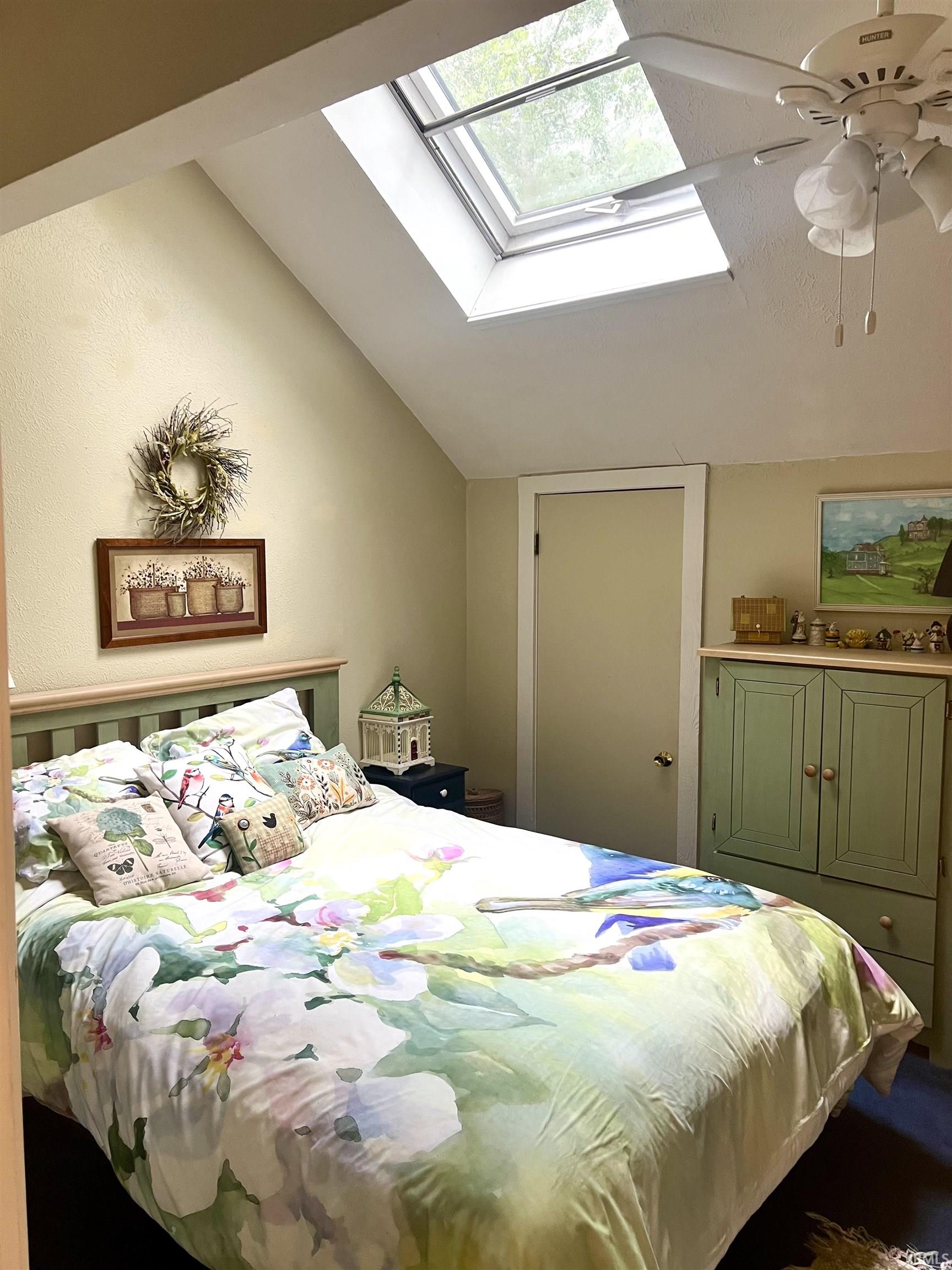 Vaulted ceiling bedroom featuring a skylight and a ceiling fan with integrated lighting