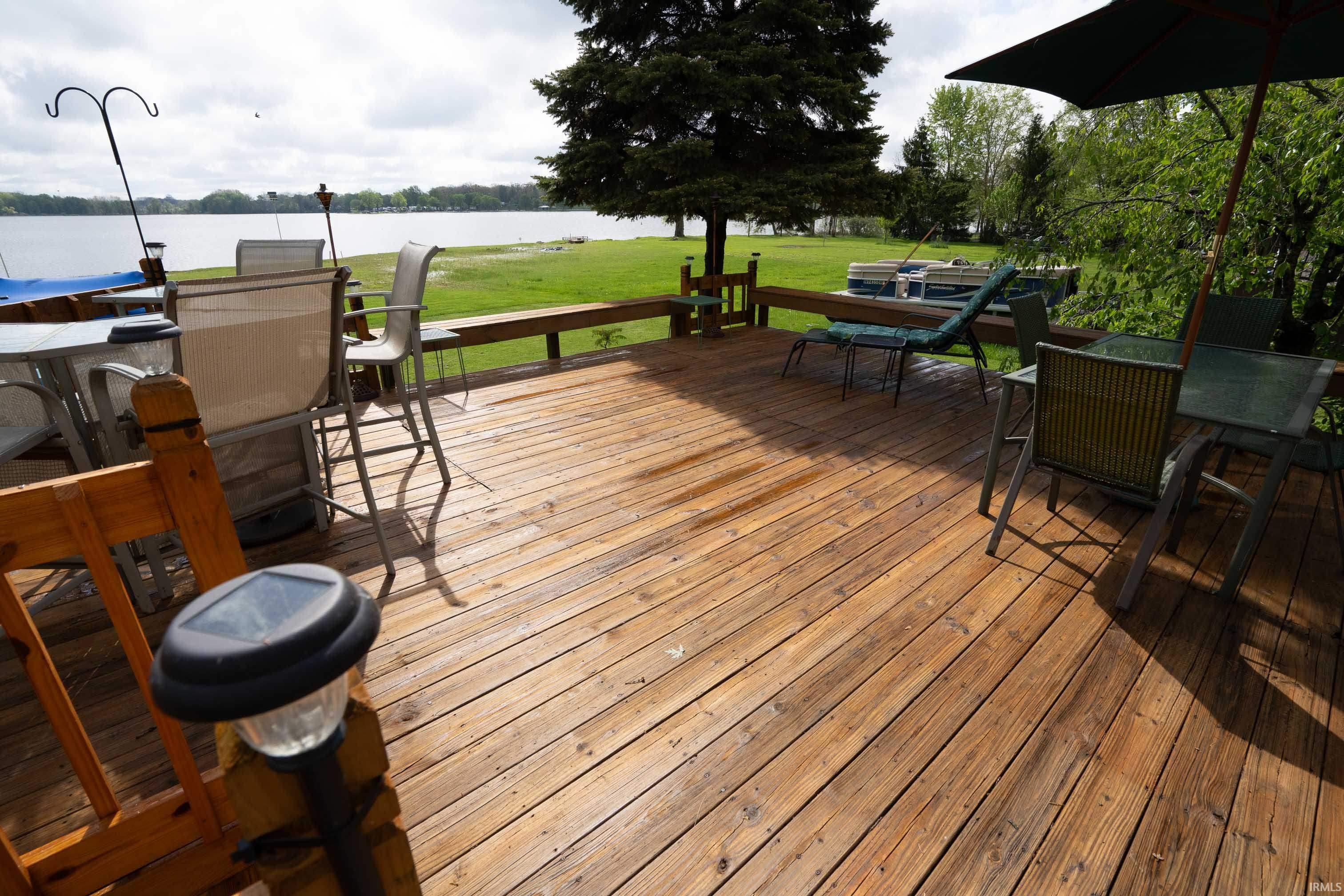 Expansive wood deck with a water frontage, featuring a lakeside lawn, and mature trees
