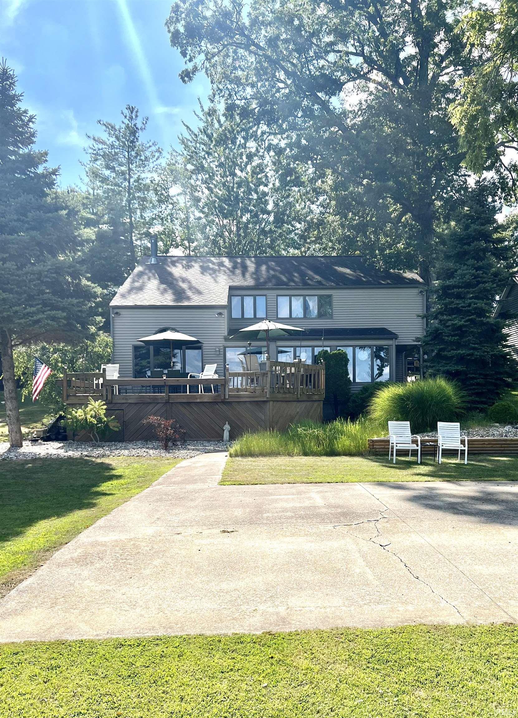 Expansive rear exterior featuring a multi-level wood deck, abundant windows, and mature perimeter trees