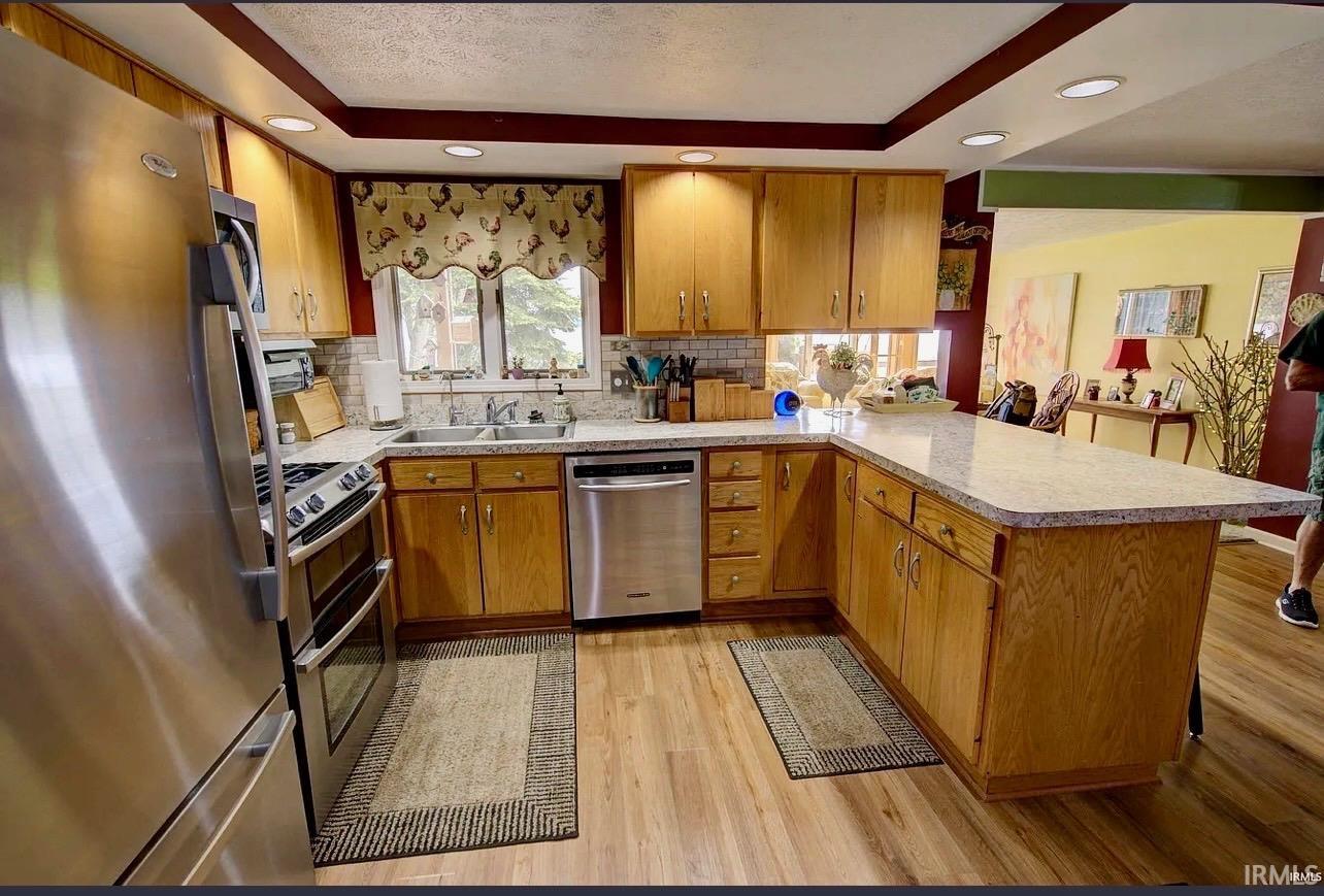 Kitchen featuring light wood cabinetry, stone-look countertops, and stainless steel appliances including a refrigerator, range, and dishwasher
