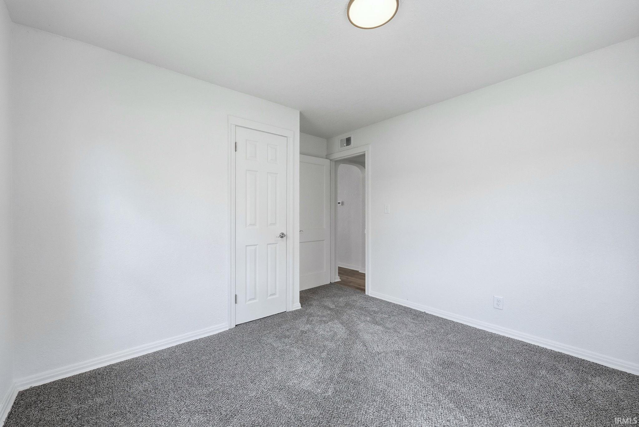 Room featuring plush grey carpeting, white painted walls, and a multi-panel interior door