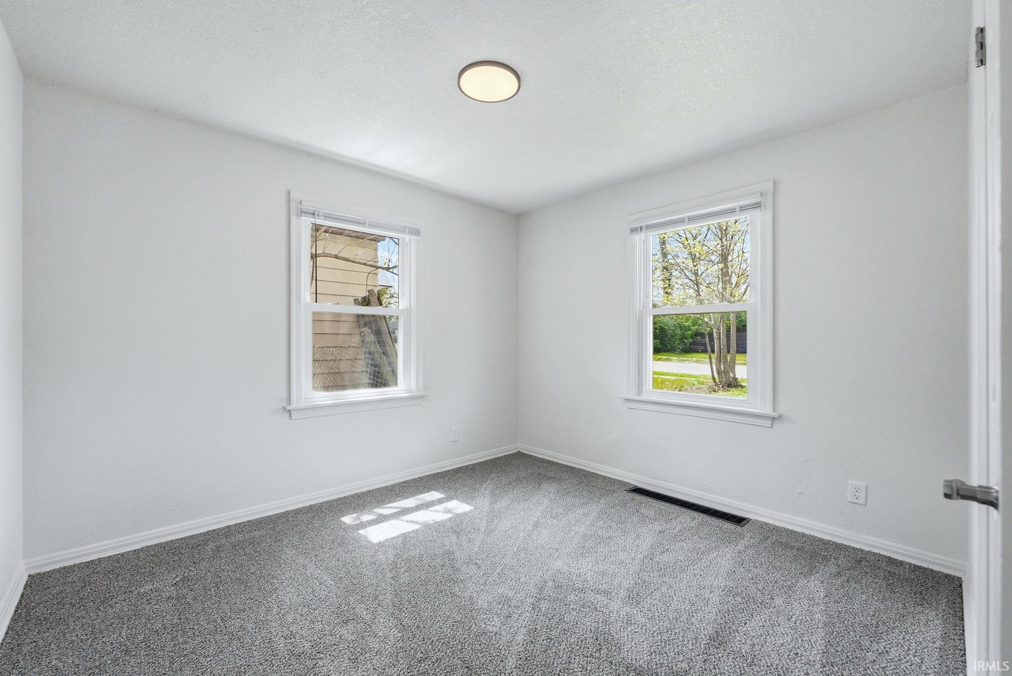 Bright room featuring two windows, light gray carpeting, crisp white walls, white trim, and a flush-mount ceiling light fixture