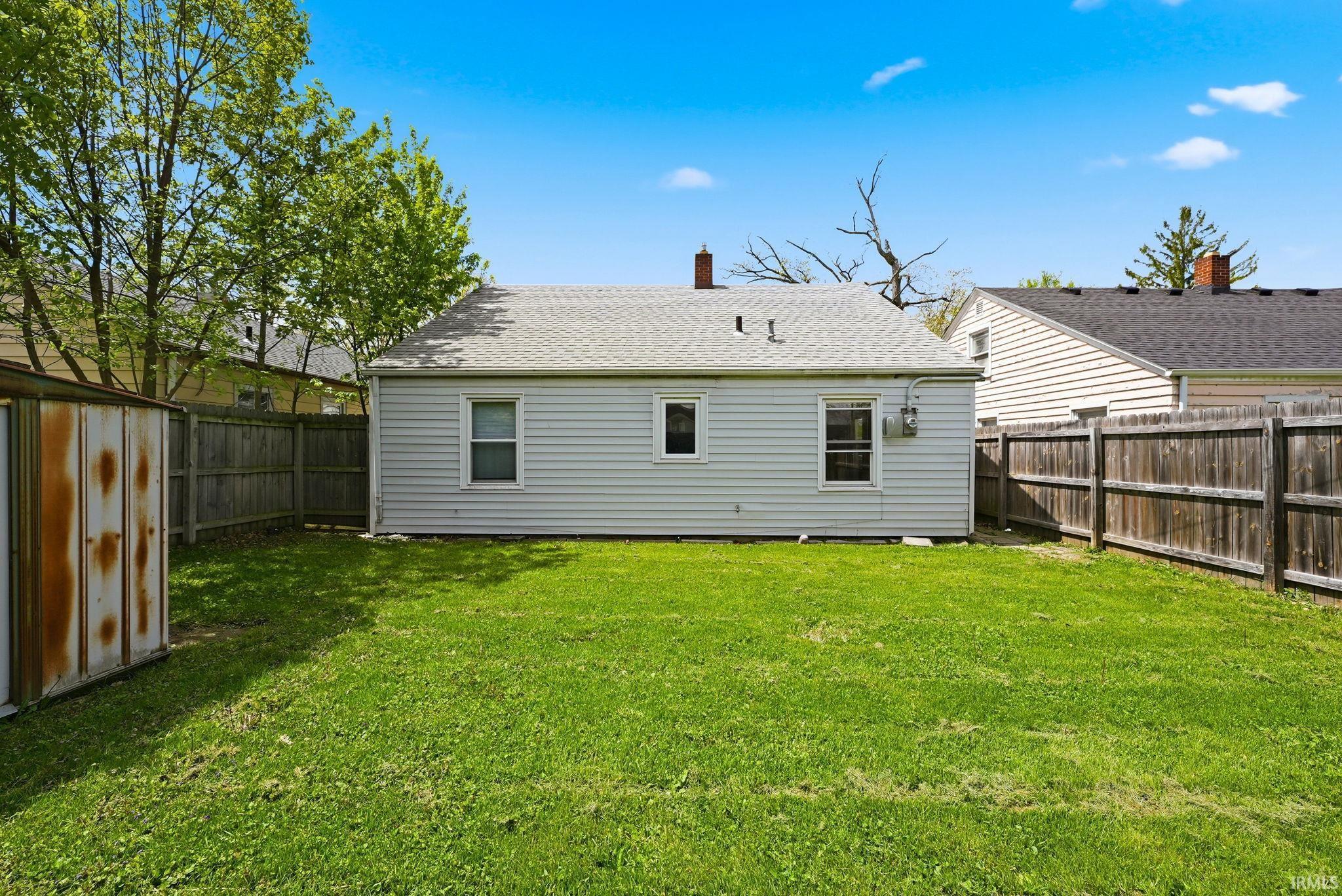 Expansive grassy backyard featuring a perimeter wood fence and a storage shed