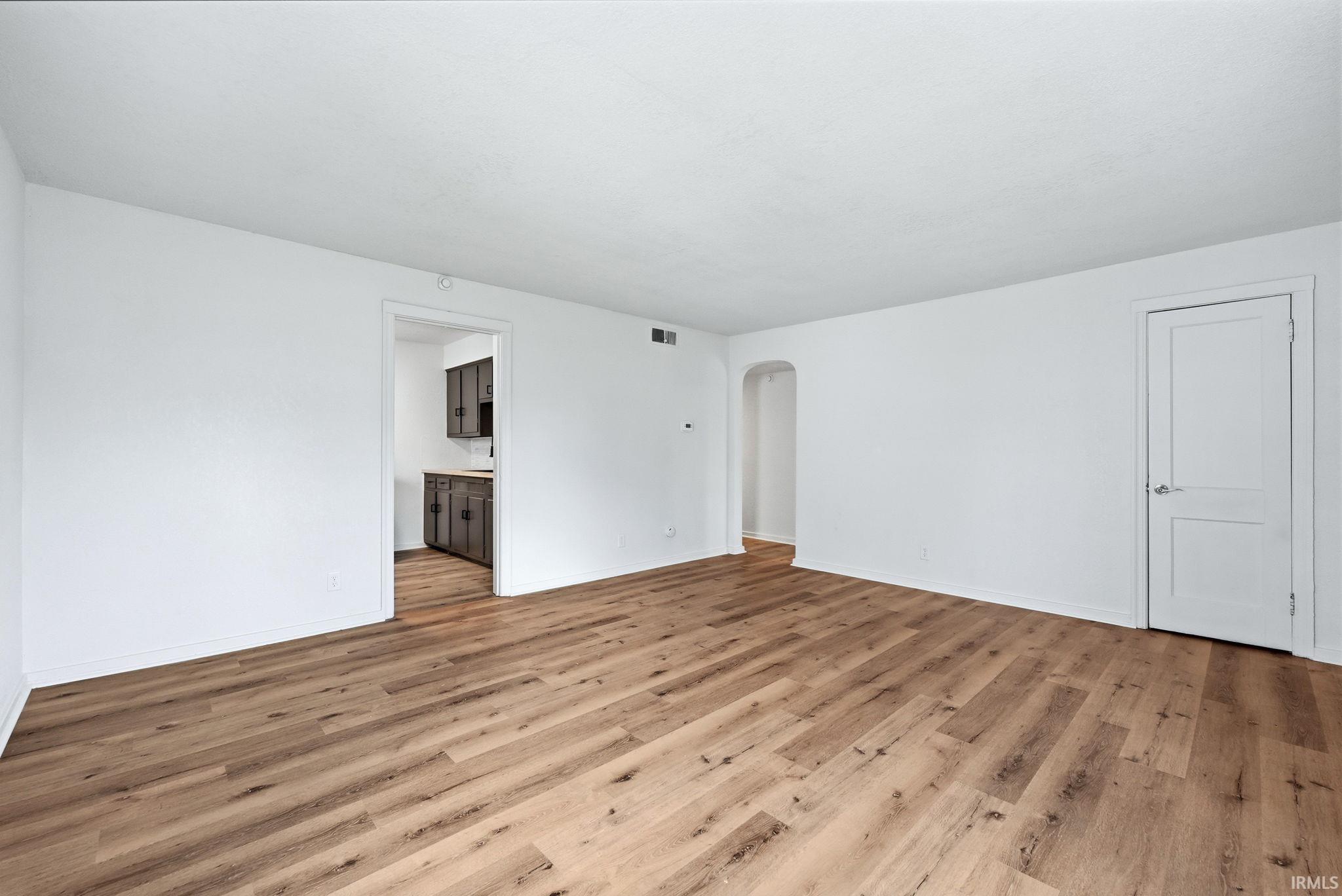 Spacious room featuring wood-finish flooring, white walls, and a recessed archway