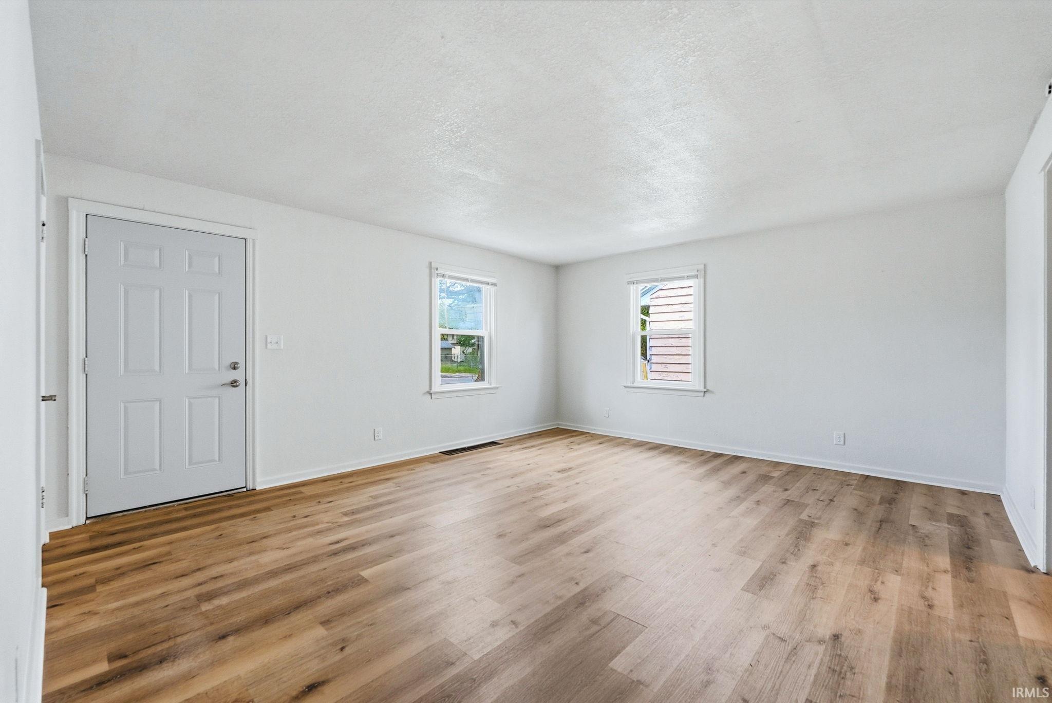 Bright interior space featuring wood-finish flooring, white walls, and two windows with natural light