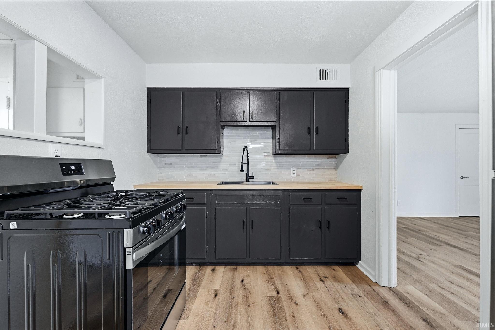 Kitchen featuring black cabinetry, light wood-finish countertops, and a white subway tile backsplash