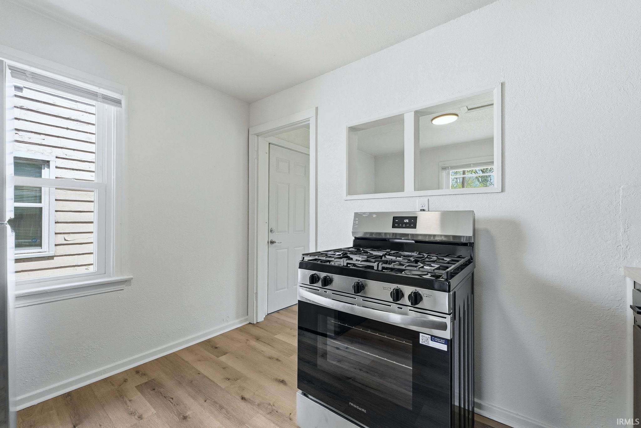 Kitchen area featuring a stainless steel range with gas burners, wood-finish flooring, and white painted walls