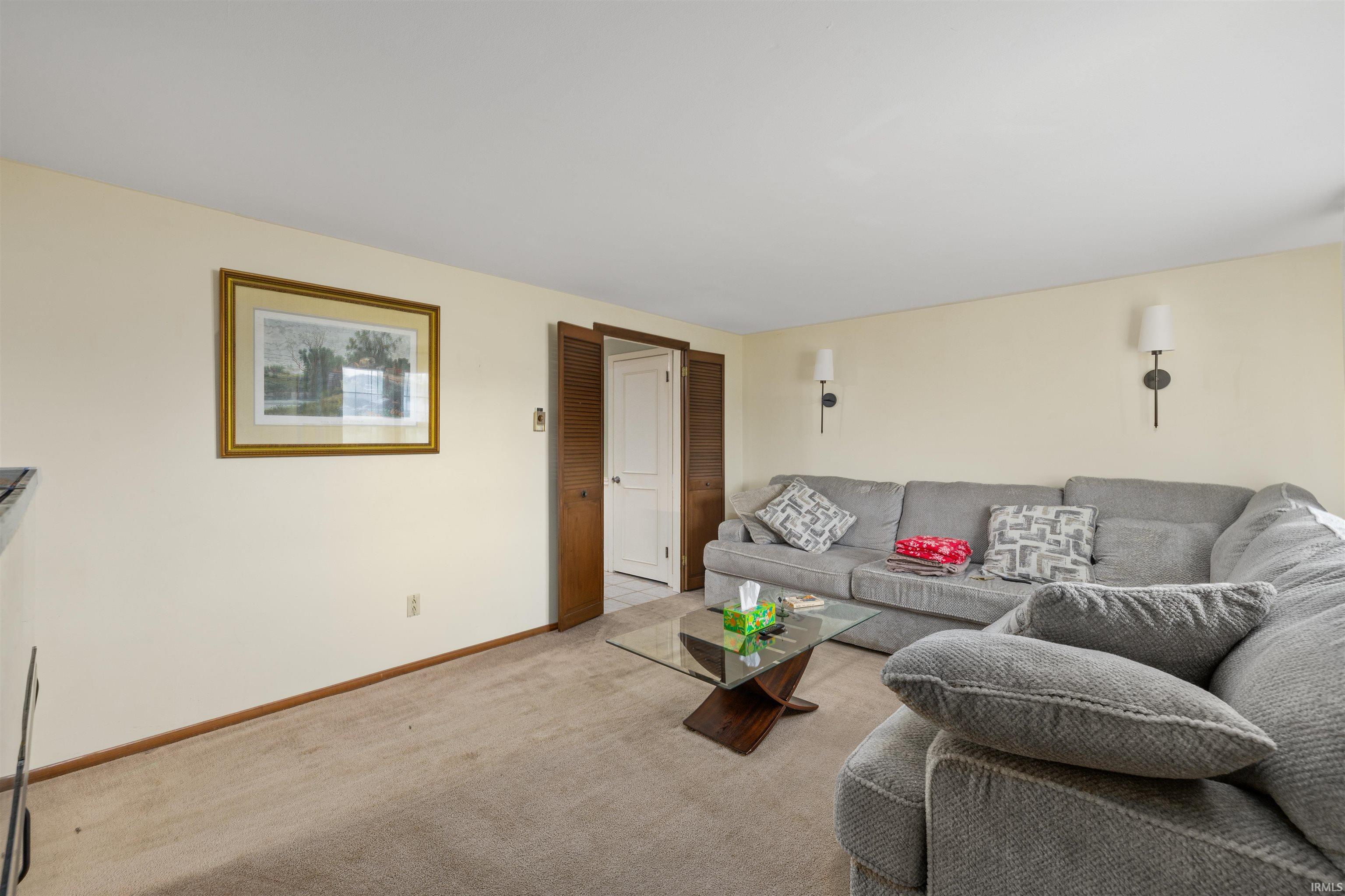 Carpeted living area featuring neutral-toned walls, two wall-mounted sconces, and a wood-finish door frame leading to another room