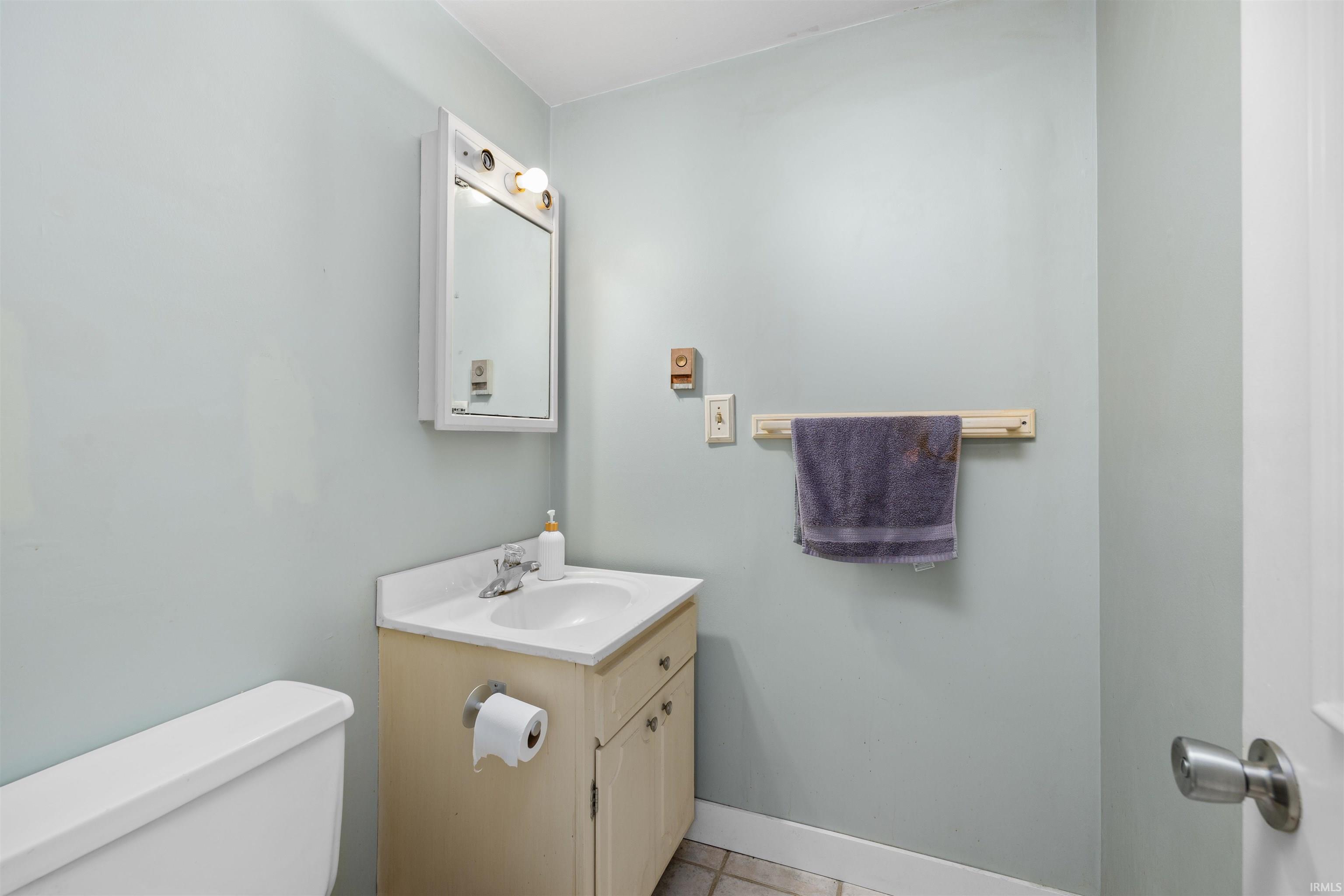 Compact bathroom featuring a white toilet, light-colored vanity with a white countertop and integrated sink, a mirrored medicine cabinet with overhead lighting, and pale blue wall paint