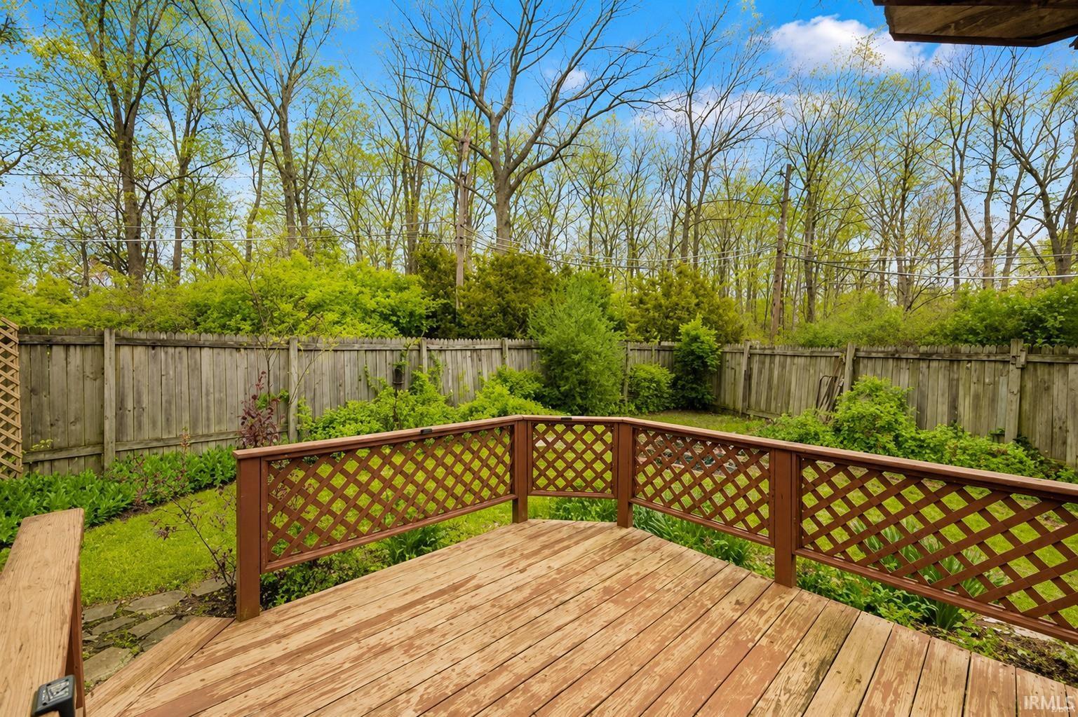 Wood-finish deck with lattice railing, surrounded by a natural wood privacy fence, and mature trees in the background