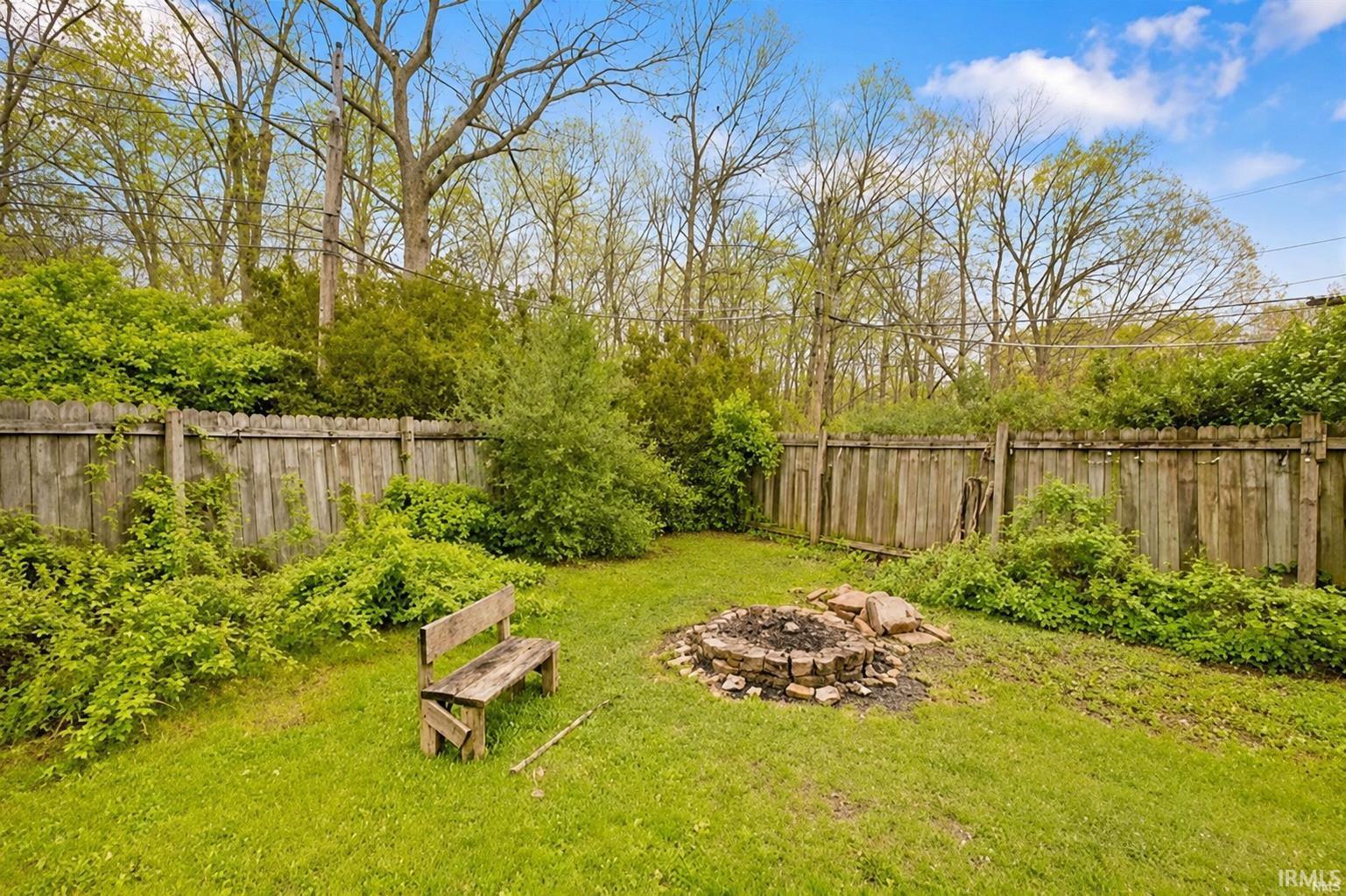 Expansive backyard featuring a manicured lawn, a wood fence perimeter, and a stone fire pit