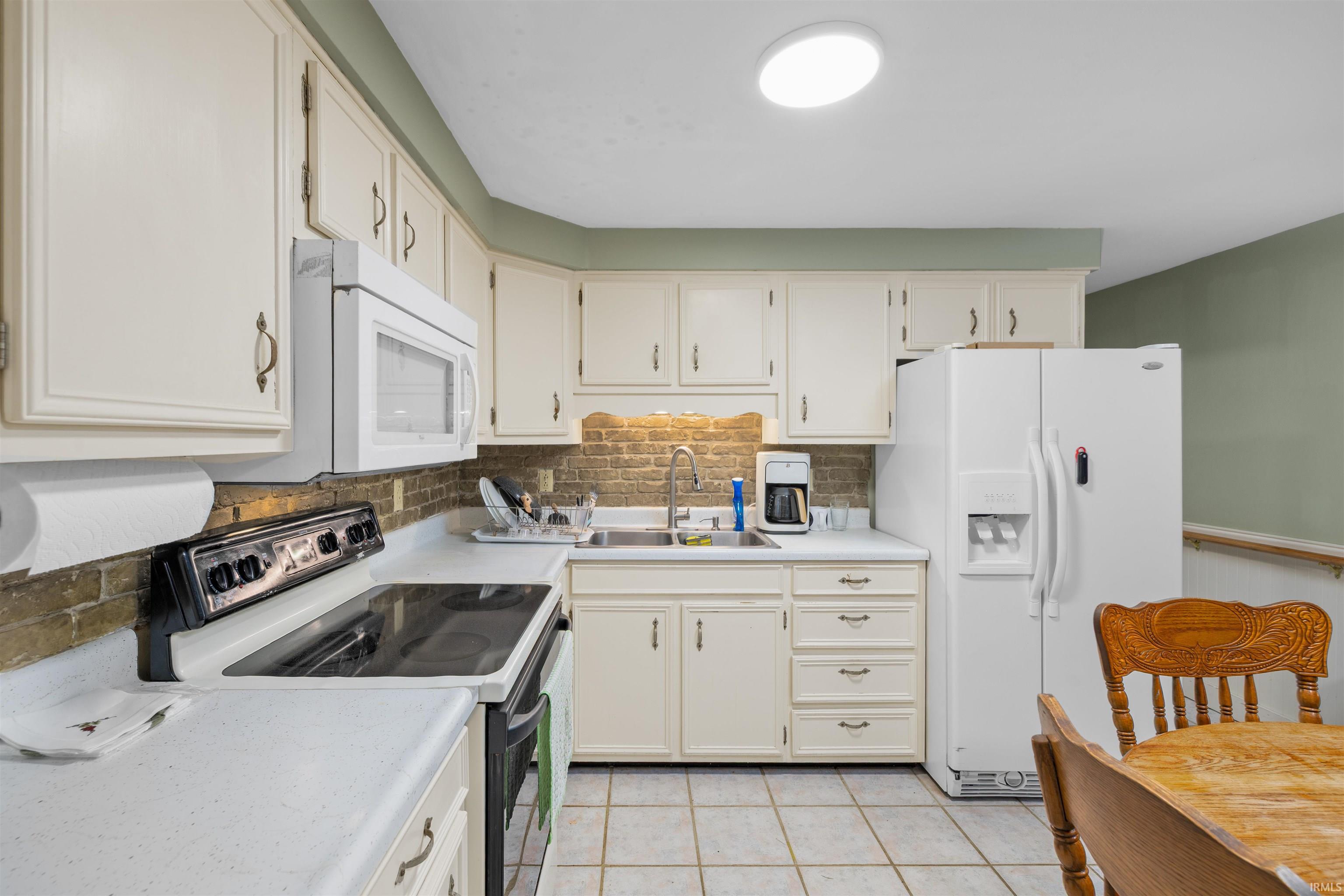 Kitchen featuring extensive white cabinetry, white countertops, tile flooring, and a brick-patterned backsplash