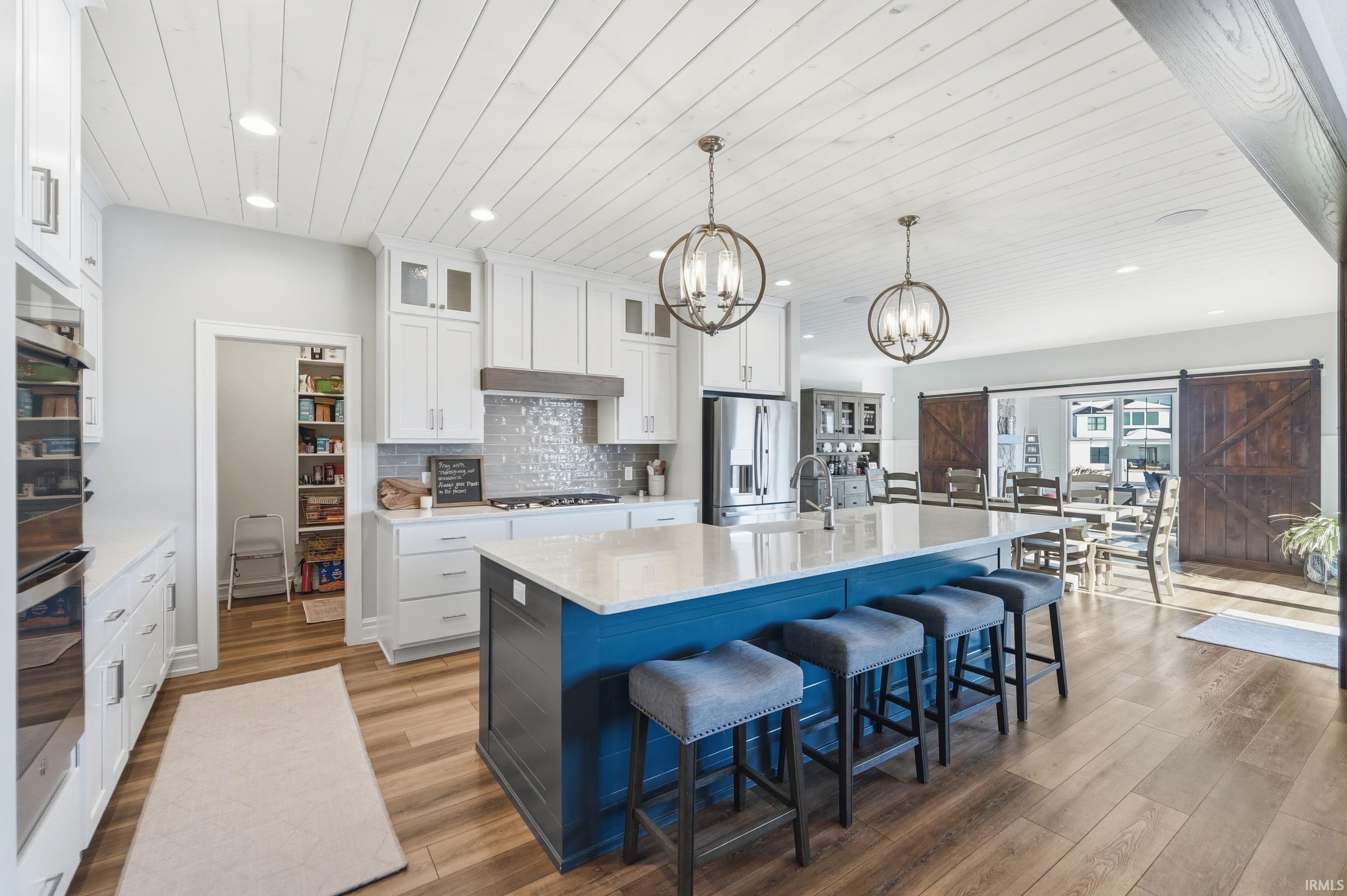 Spacious kitchen featuring an expansive island with seating, white shaker cabinetry, stainless steel appliances, and wood-finish flooring