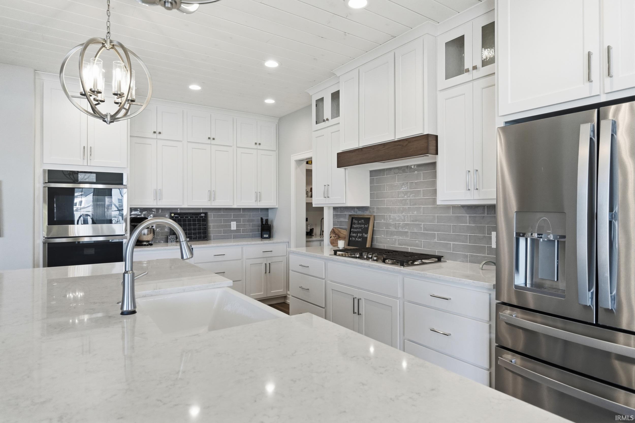 Gourmet kitchen featuring white cabinetry, light-toned countertops, stainless steel appliances, a tile backsplash, and a large central island with an undermount sink