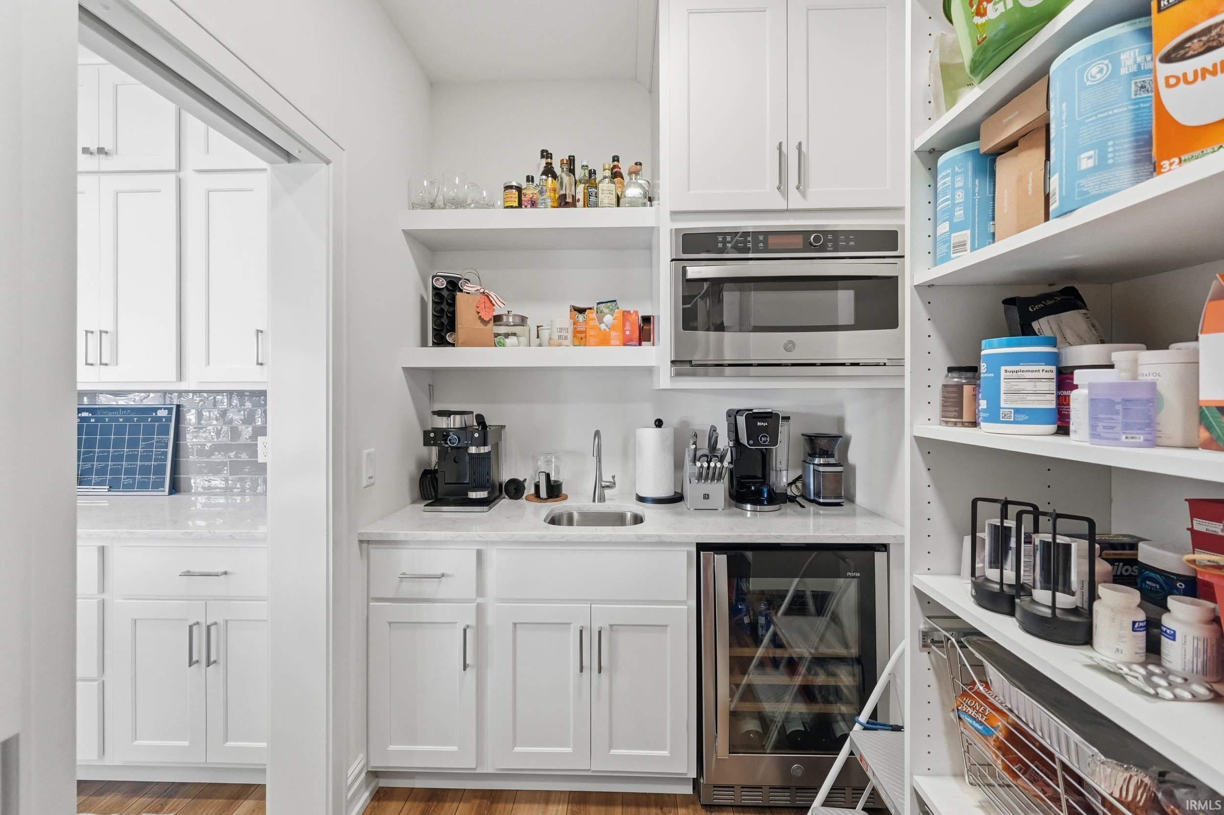 White cabinetry kitchen area with built-in stainless steel microwave, integrated beverage cooler, and a single basin sink