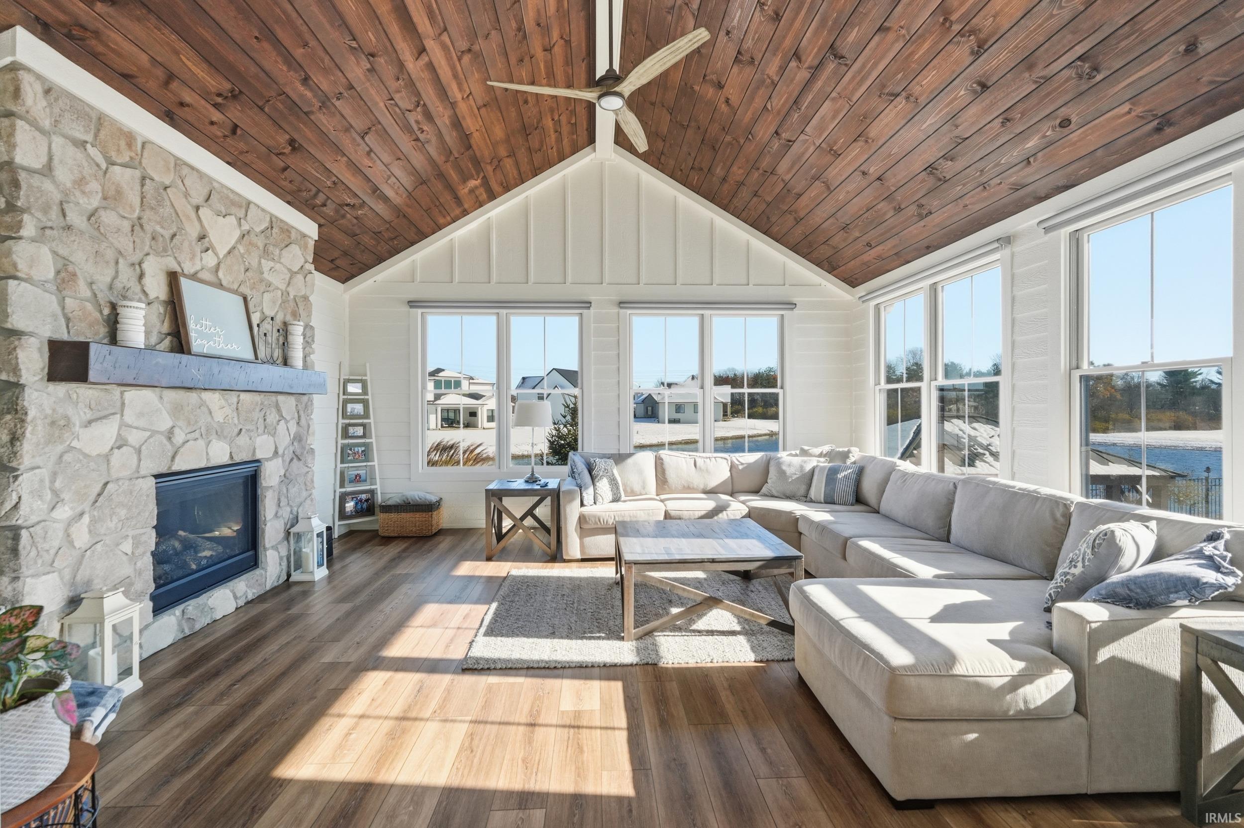 Vaulted wood-plank ceiling room featuring a stone fireplace with a wood mantle, wood-finish flooring, and multiple windows