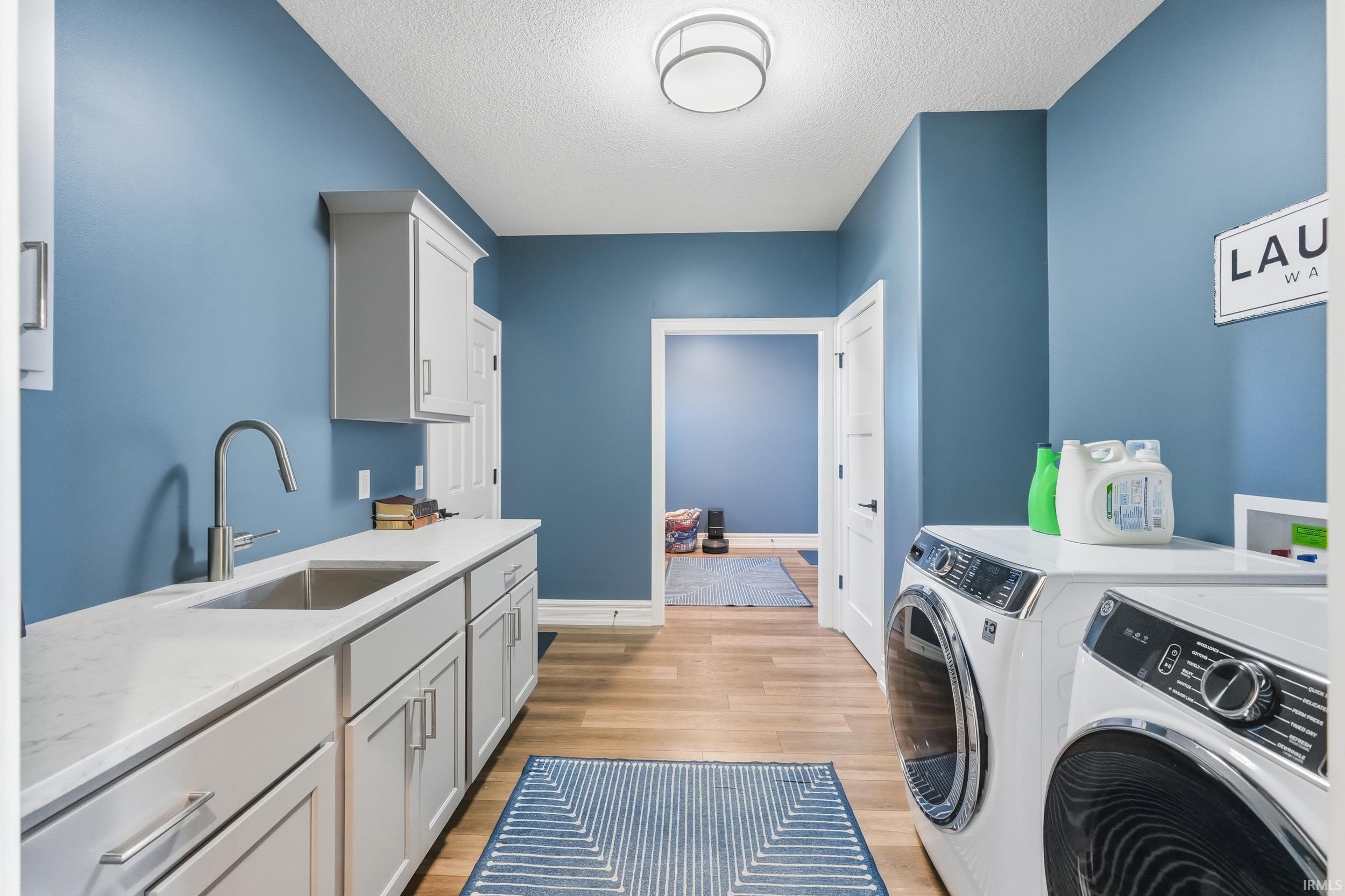 Laundry room featuring a built-in sink with a gooseneck faucet, light grey cabinetry, white countertops, and wood-finish flooring