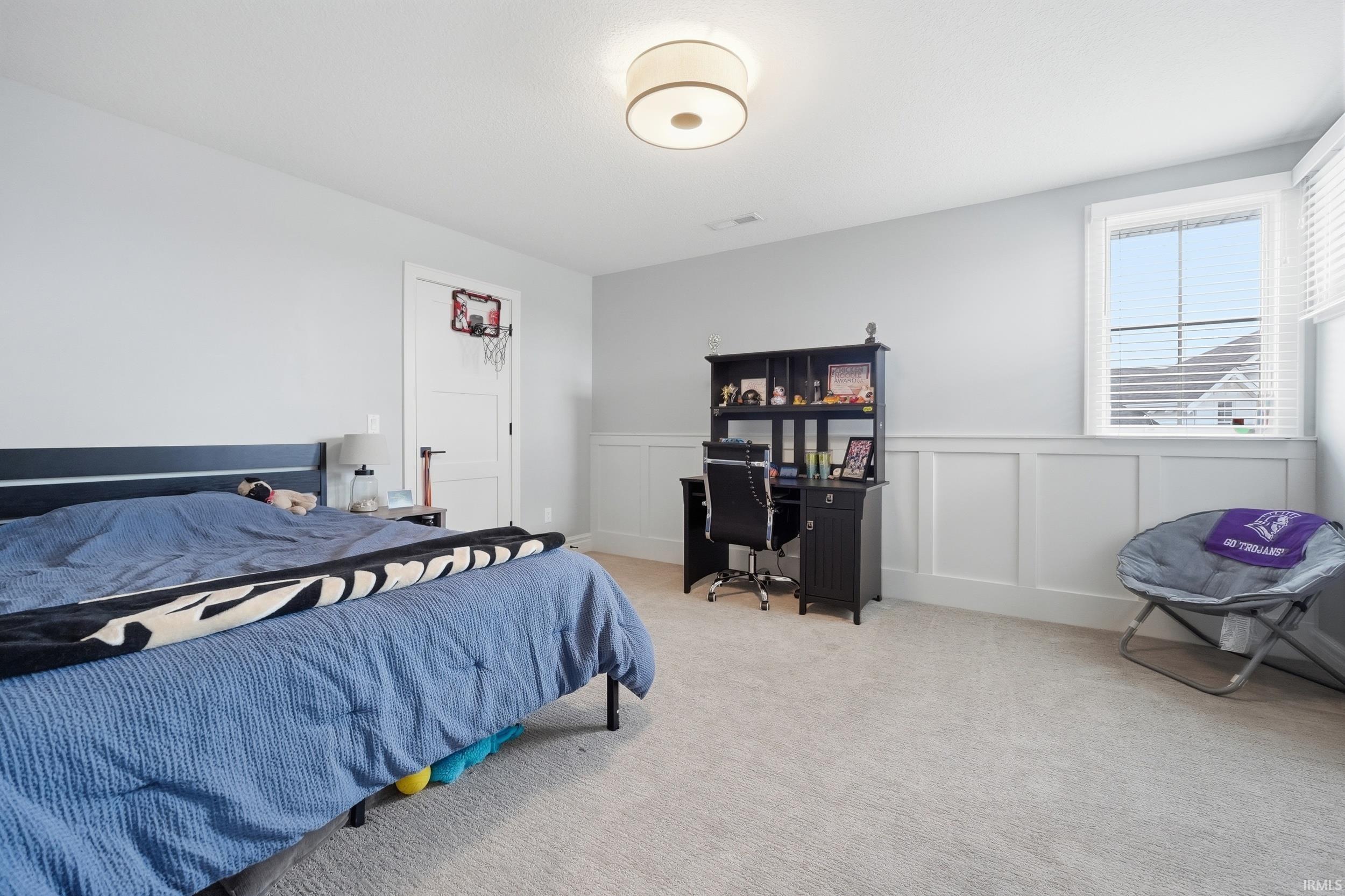 Bedroom featuring light gray walls, white board and batten wall treatment, light carpet flooring, and a flush mount ceiling light fixture
