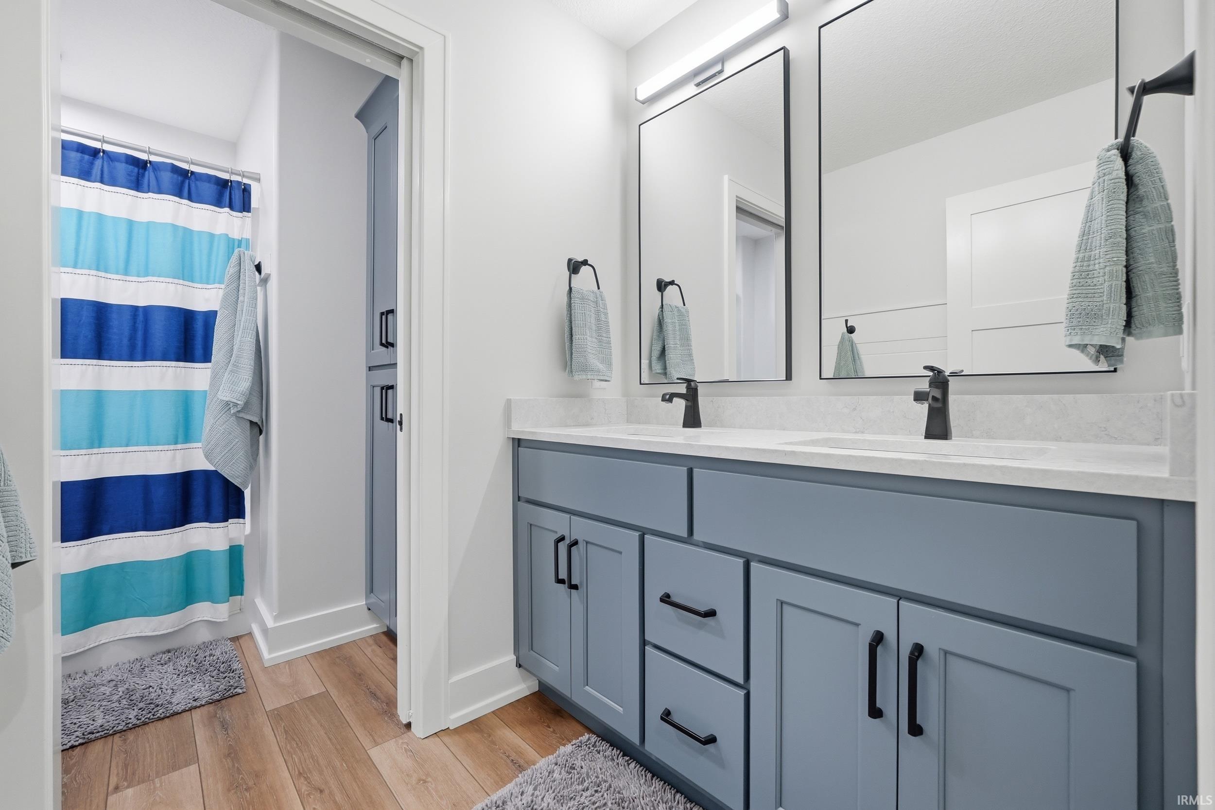 Dual vanity featuring light blue cabinetry with matte black hardware, white countertops, and two rectangular mirrors with black frames