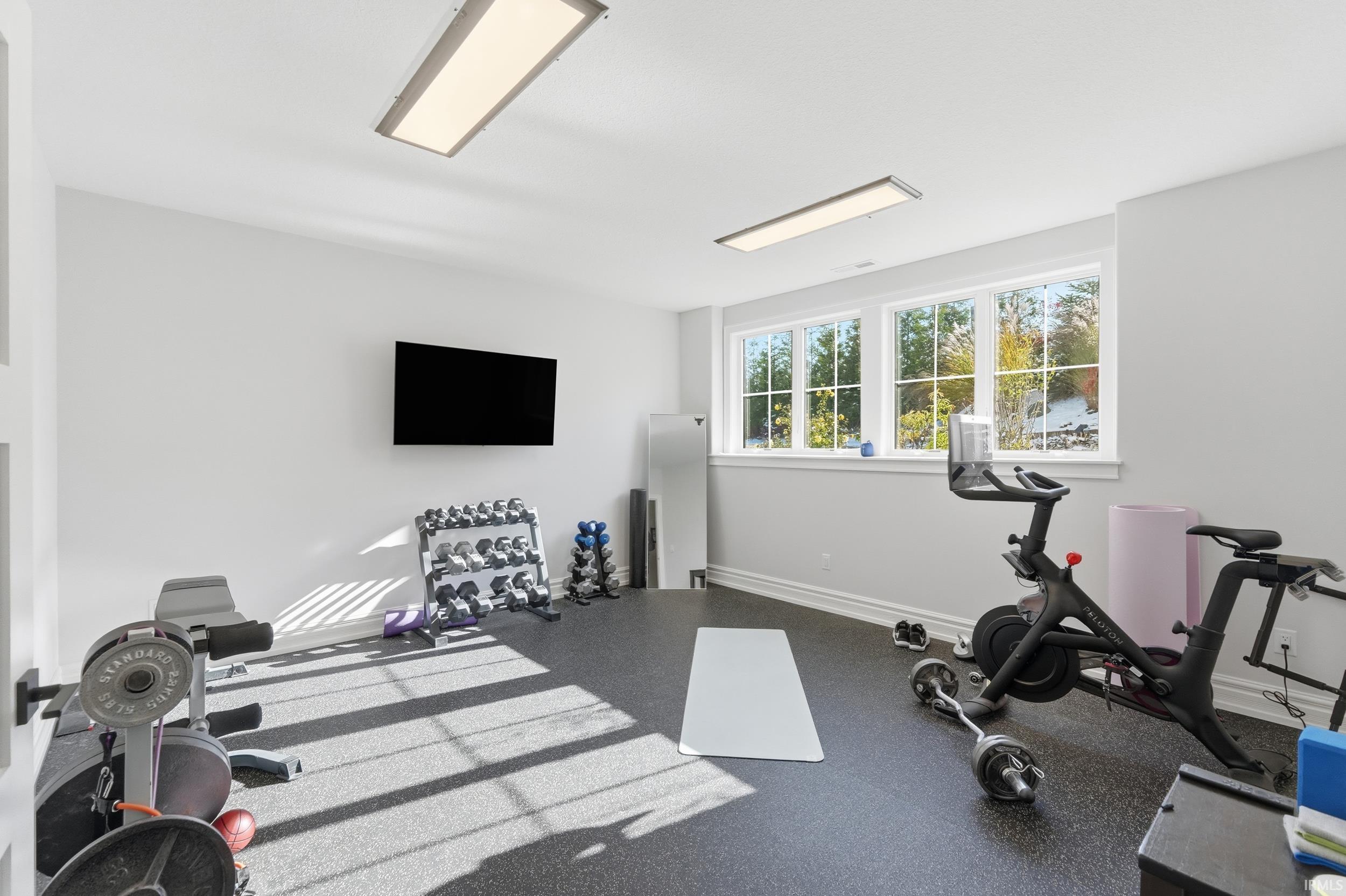 Spacious room featuring three large windows, recessed ceiling lighting, a wall-mounted television, and durable rubber flooring