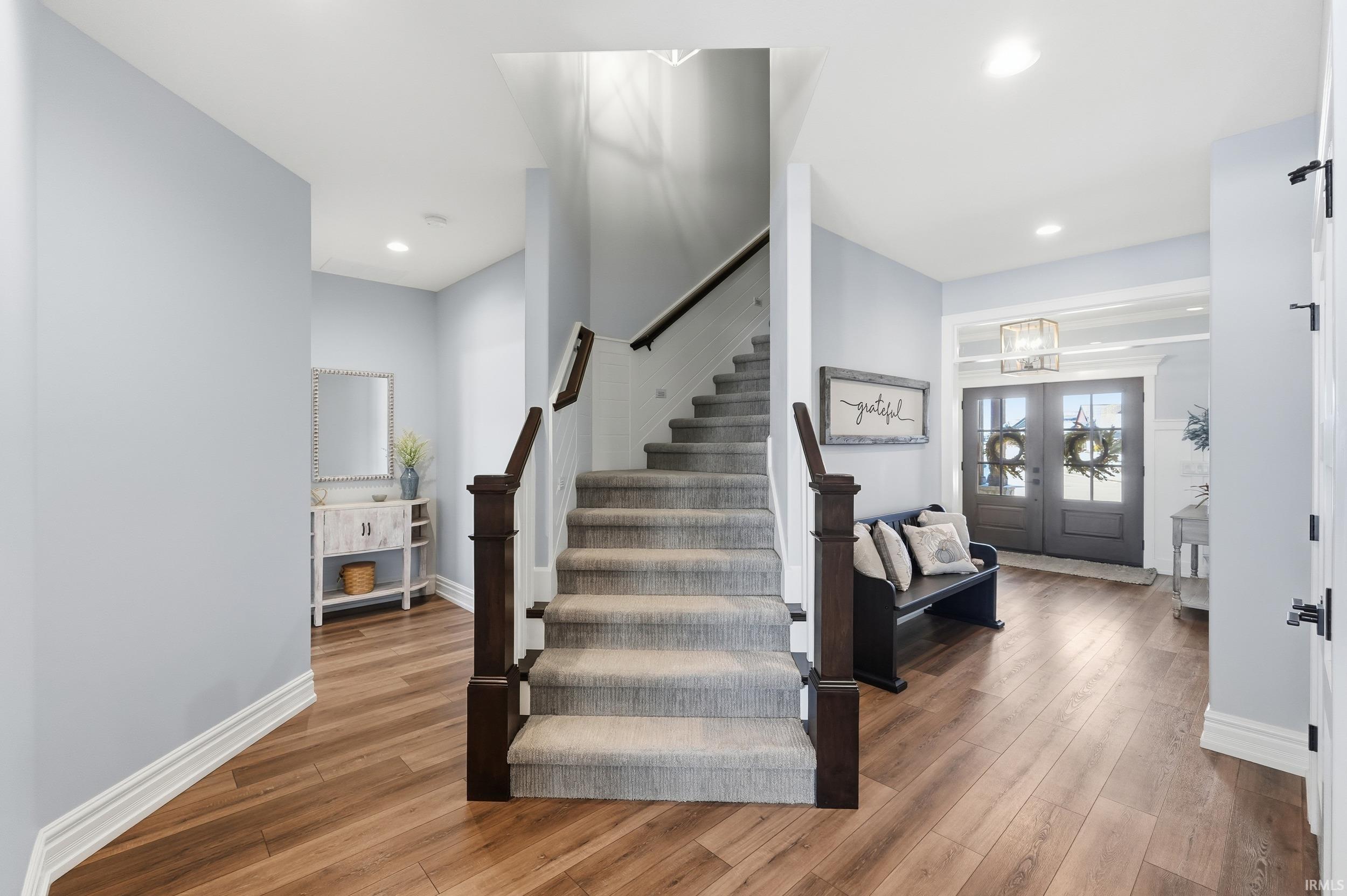 Wood-finish flooring throughout the entryway, featuring a carpeted staircase with dark wood newel posts and handrail