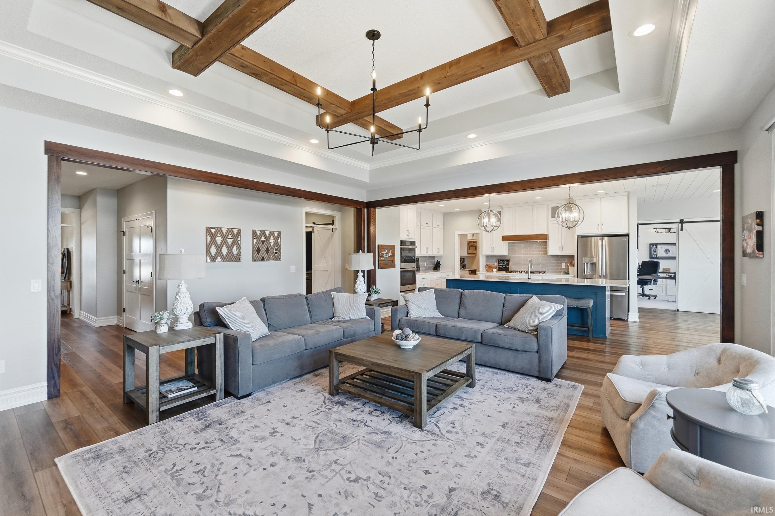 Expansive living space featuring a tray ceiling with wood beams, recessed lighting, and a modern chandelier