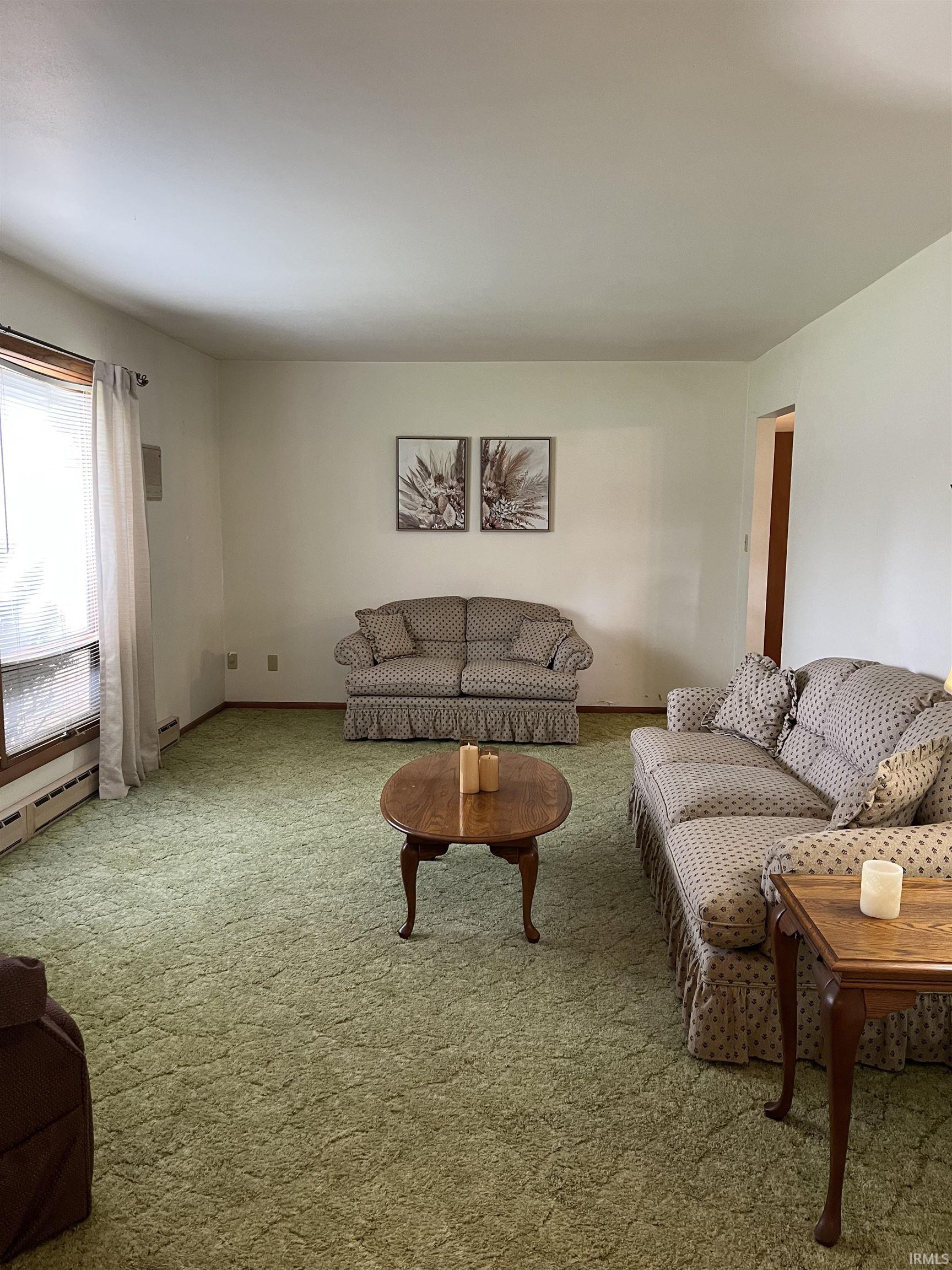 Spacious living area featuring light-toned walls and green carpeting