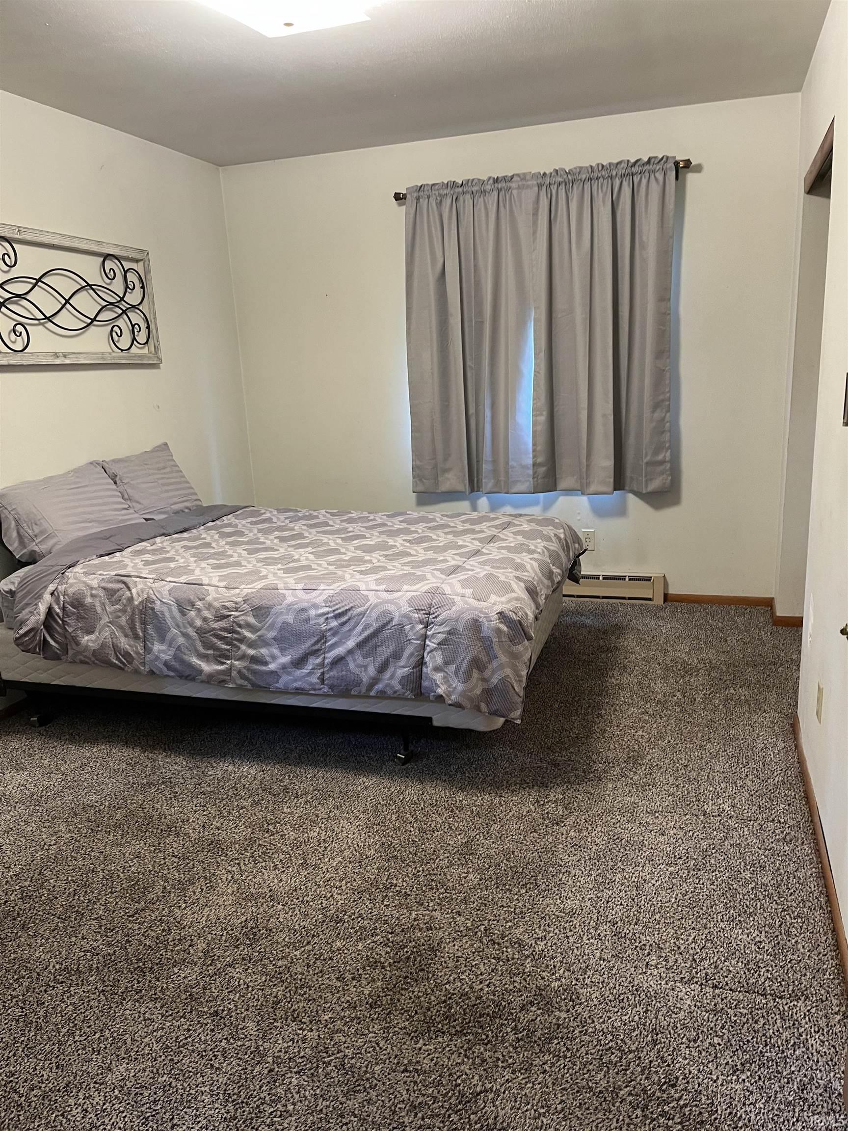 Carpeted room featuring a window with privacy curtains and a baseboard heating unit