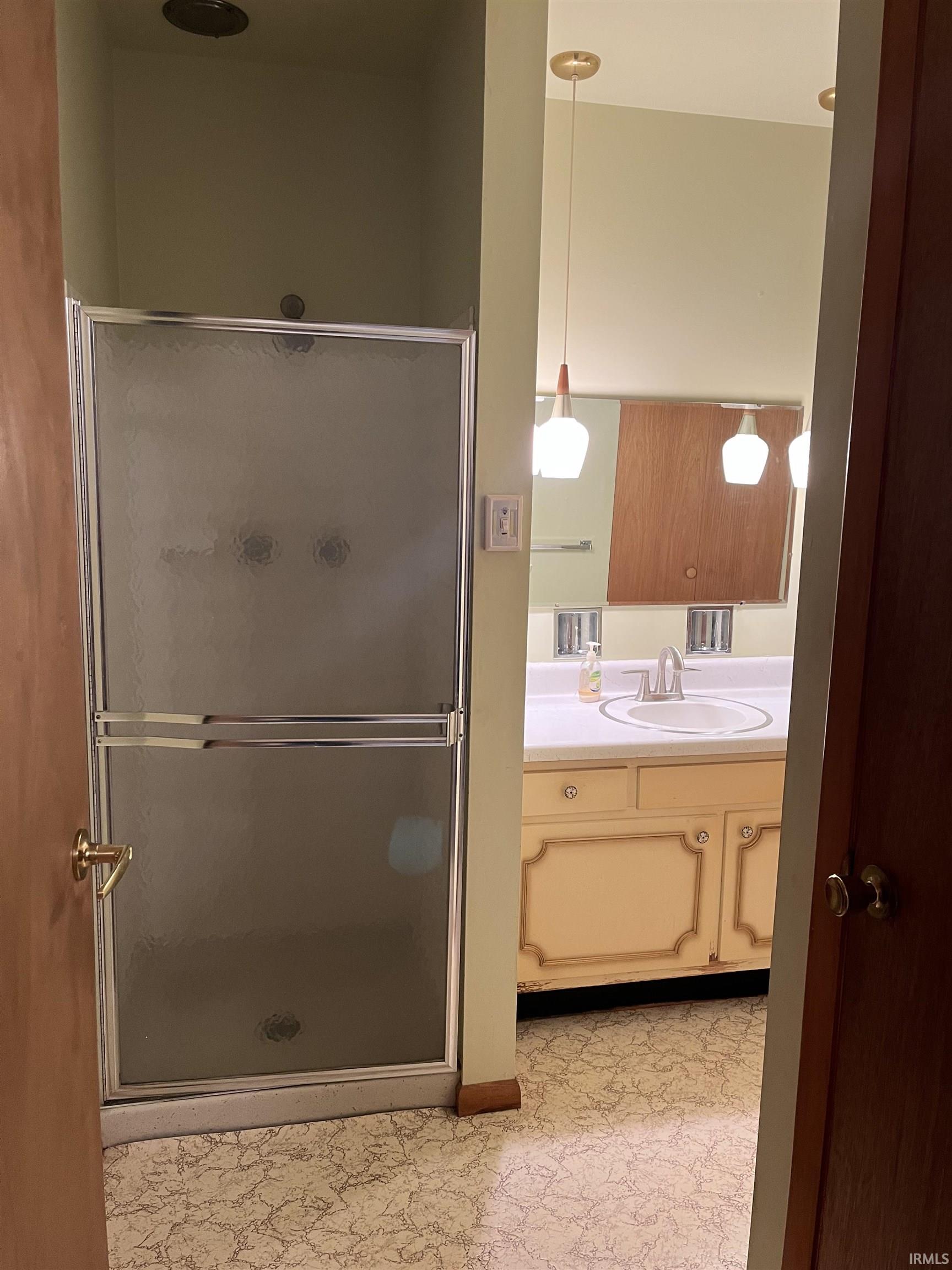 Bathroom featuring a glass-enclosed shower, a vanity with a drop-in sink, and patterned flooring