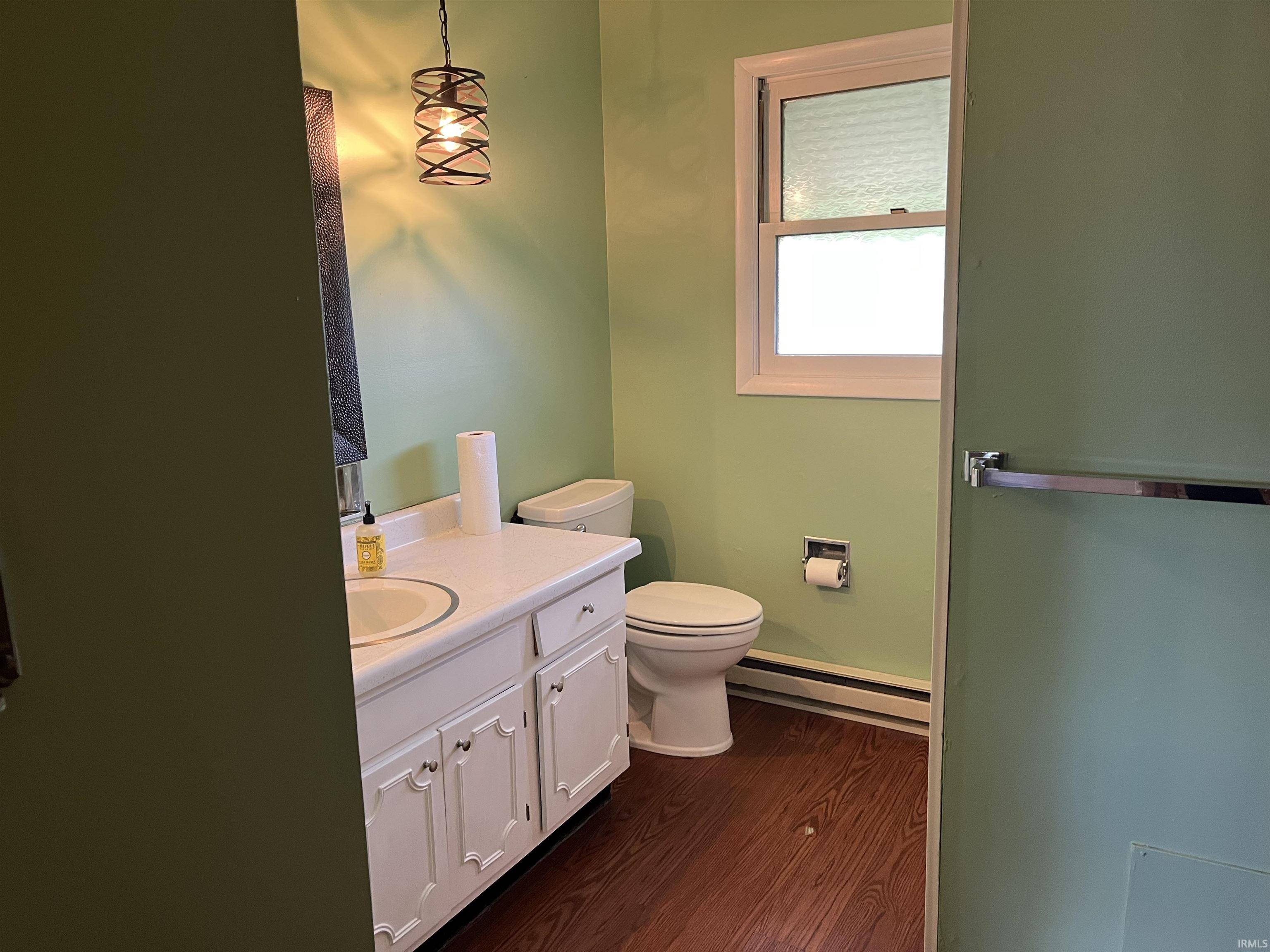 Bathroom featuring a single vanity with storage cabinetry, integrated sink, and dark wood-finish flooring