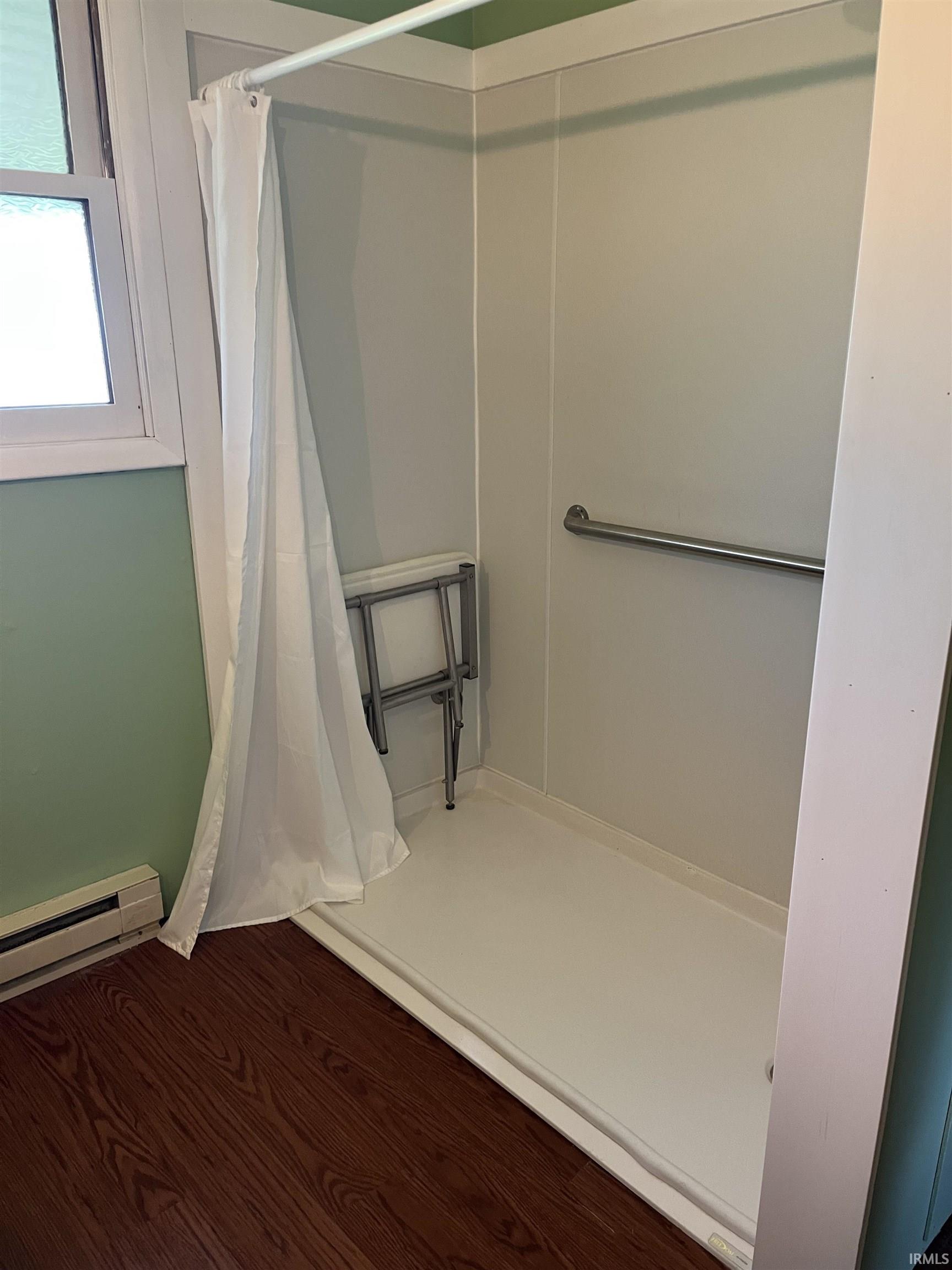 Shower stall with white wall panels, a metal grab bar, and a white shower pan