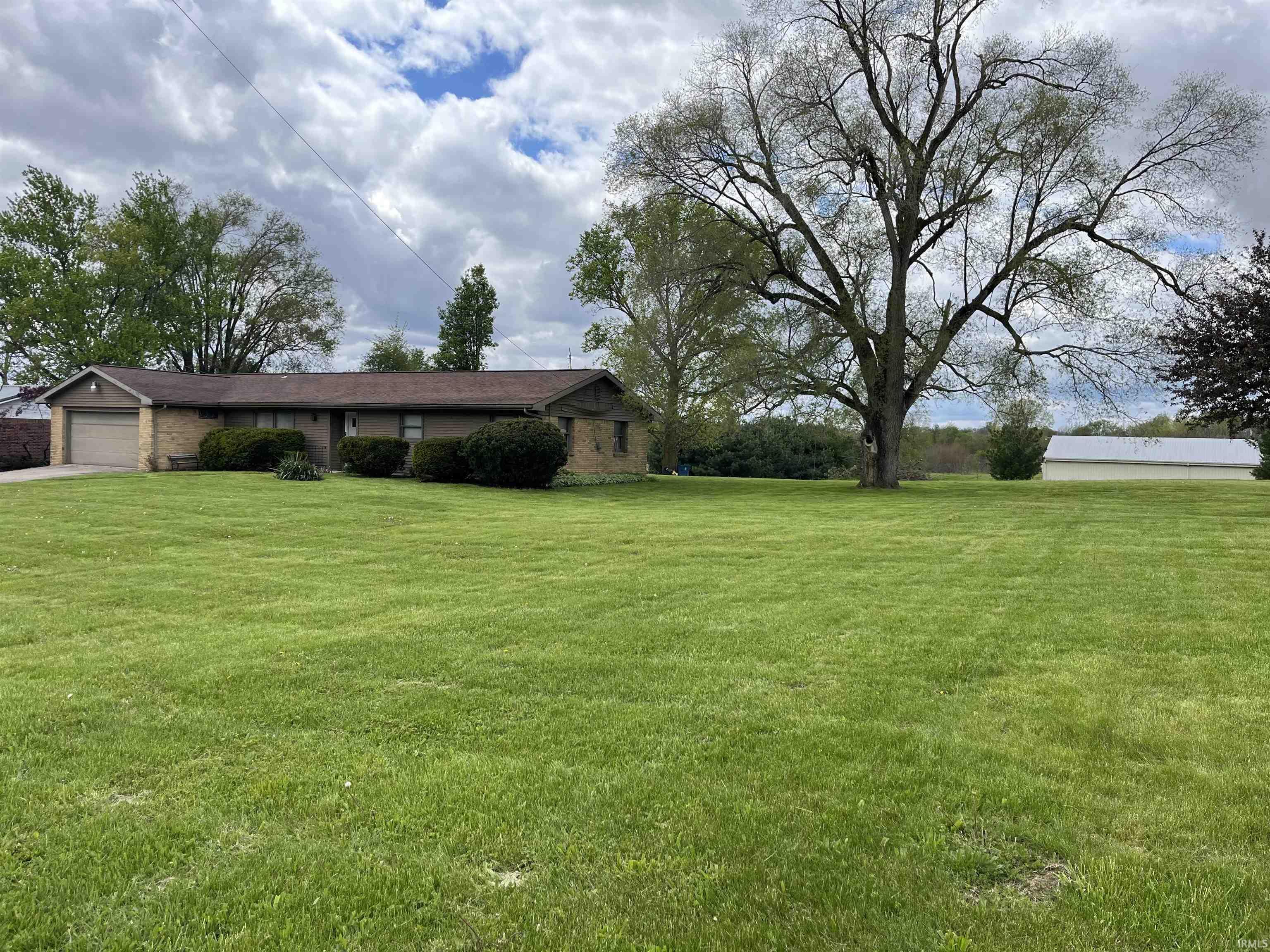 Expansive green lawn with mature trees and a single-story residence featuring a brick facade and an attached garage