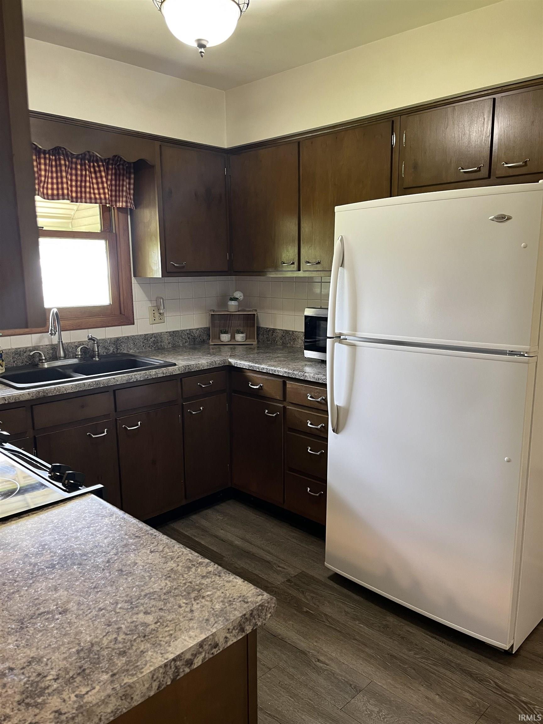 Kitchen featuring dark wood cabinetry, patterned countertops, and wood-finish flooring