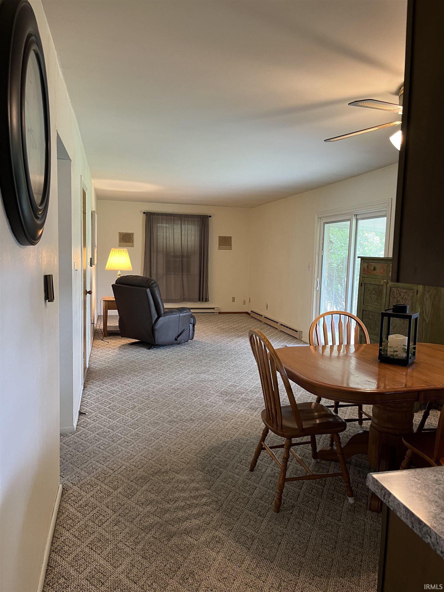 Open-concept living space featuring patterned carpet flooring, a ceiling fan, and sliding glass door access
