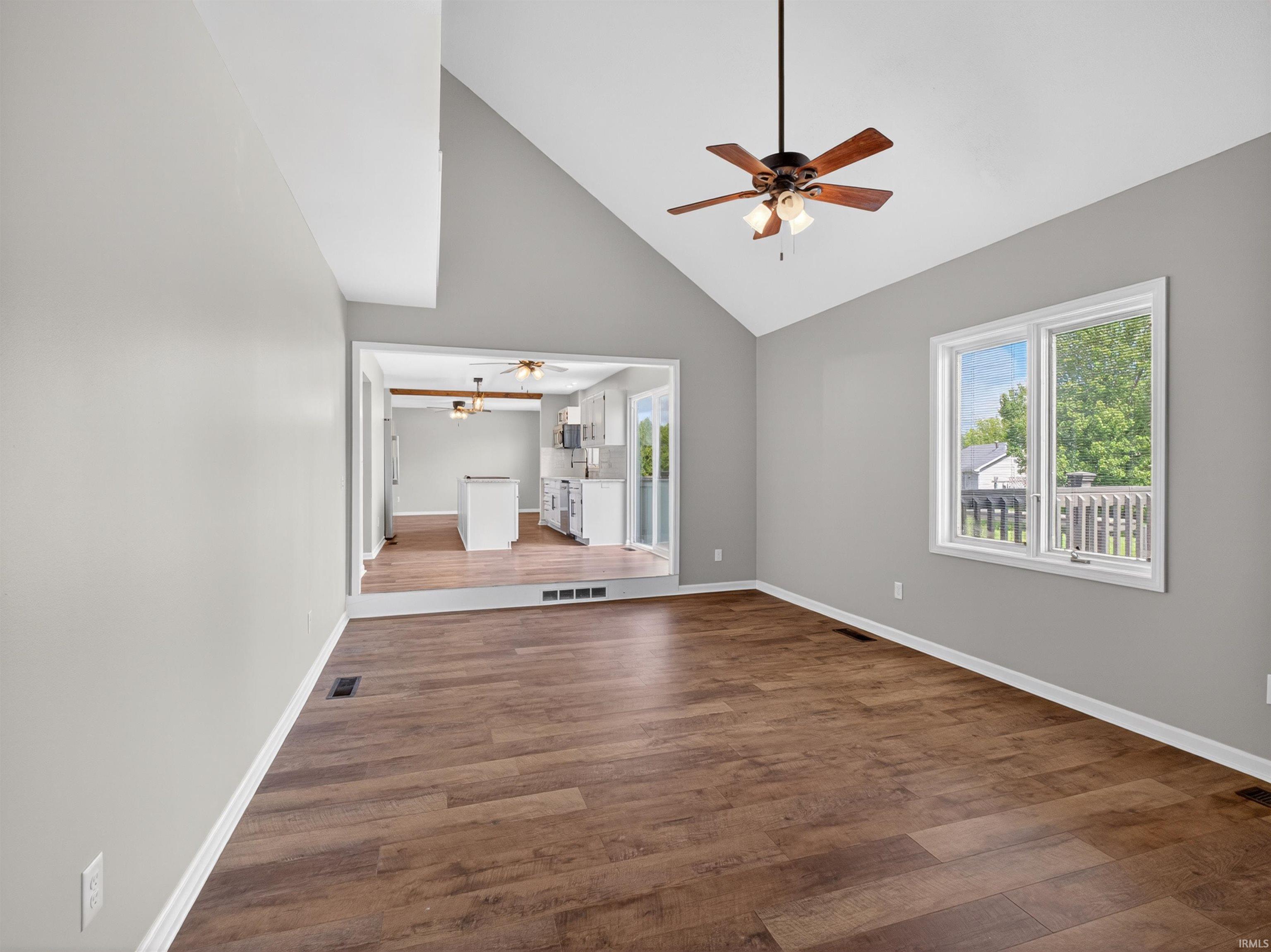 Spacious living area featuring vaulted ceilings, wood-finish flooring, a ceiling fan, and ample natural light from a large window