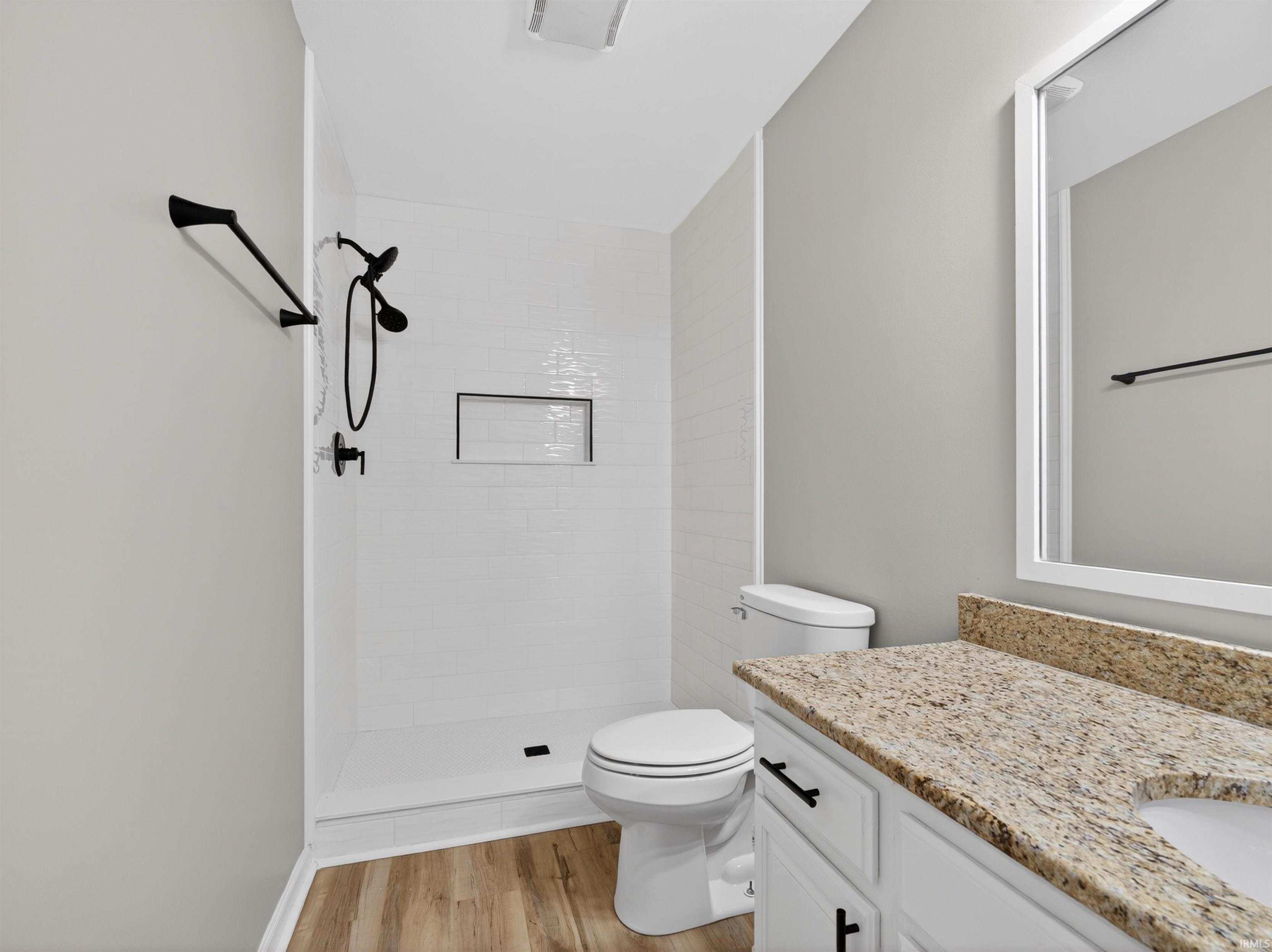 Bathroom with wood-finish flooring, a walk-in shower with white subway tile, a recessed shower niche, and matte black fixtures