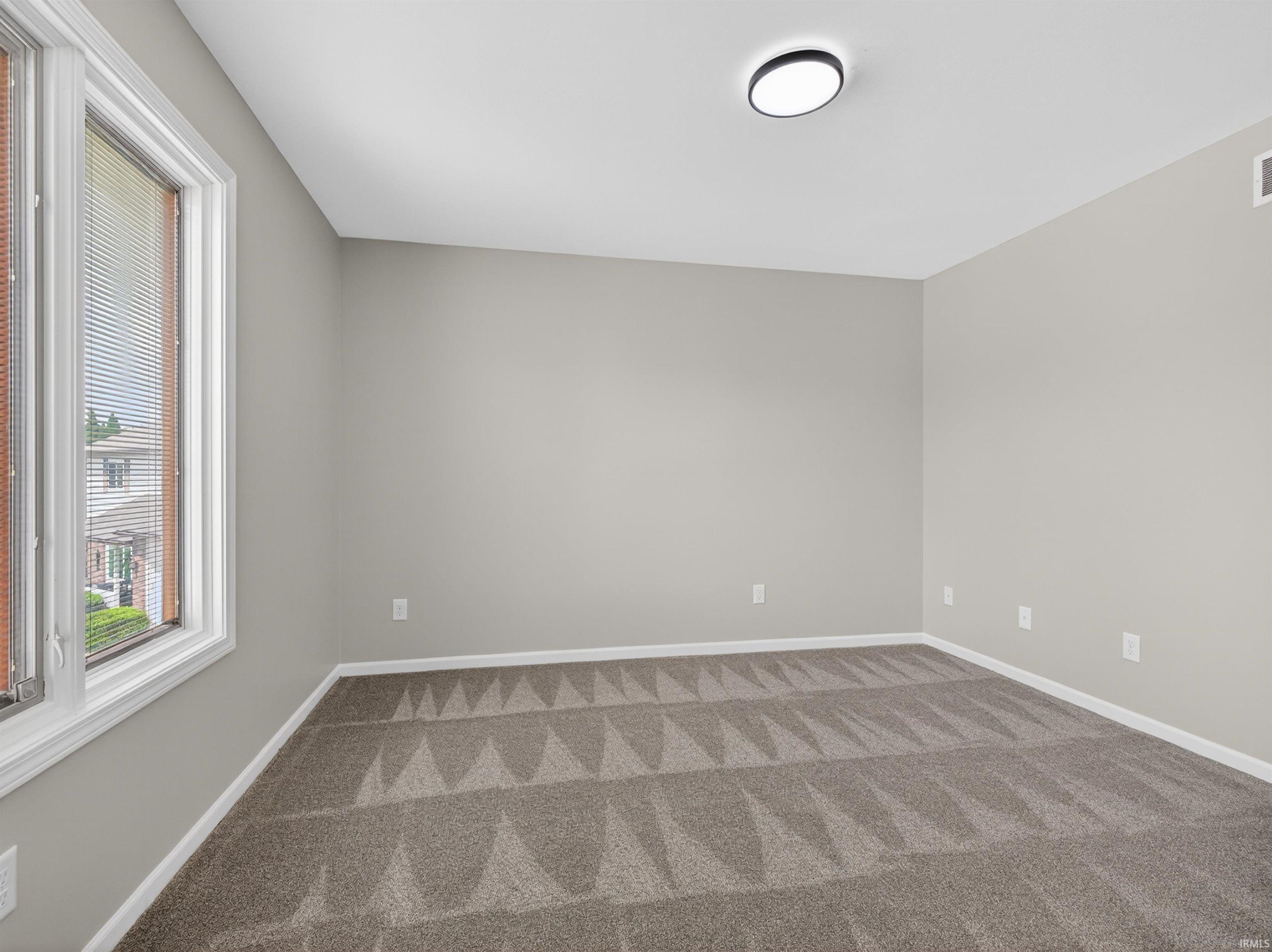 Interior room featuring neutral wall paint, patterned carpet flooring, a flush-mount ceiling light fixture, and a large window with blinds